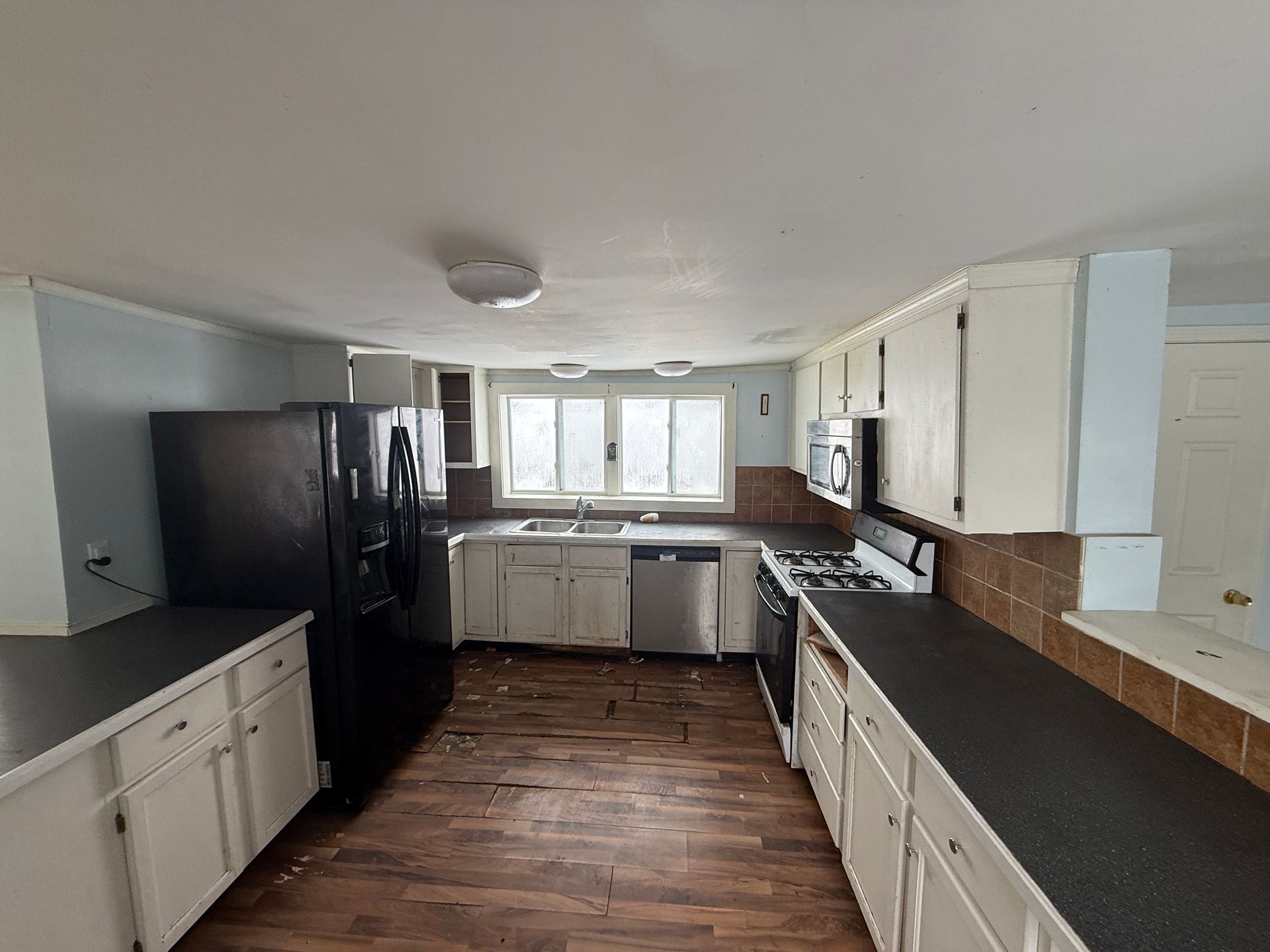 Kitchen with white cabinets, dark countertops, black refrigerator, and wood-look flooring.