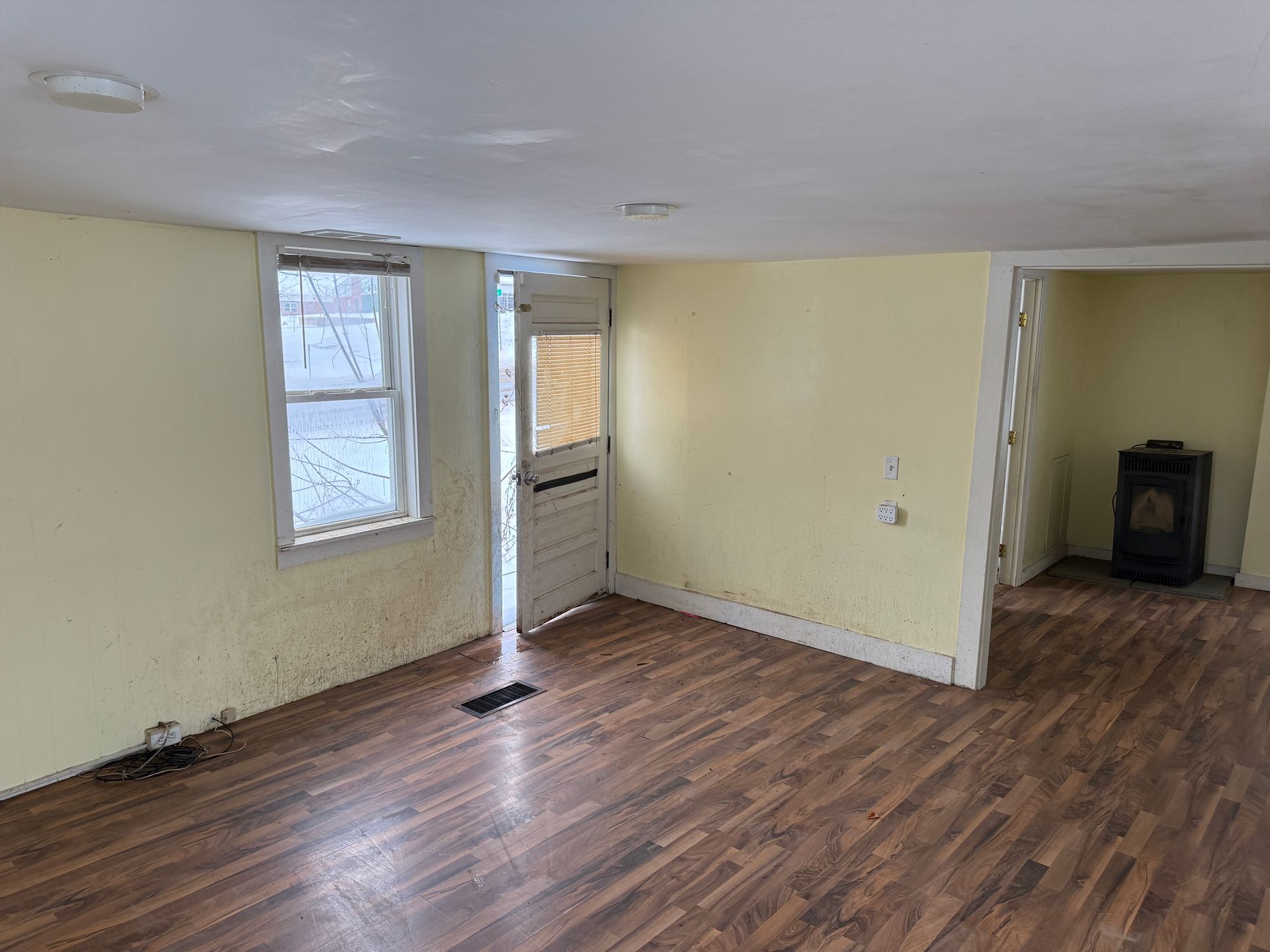 Interior of a room with yellow walls, a wooden floor, a window, and an open doorway.