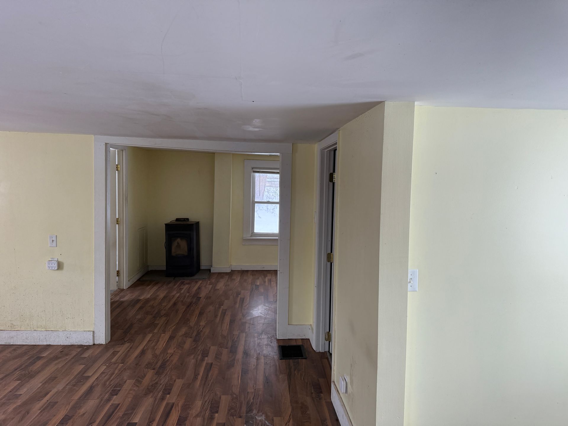 An empty room with yellow walls, dark wood-look floor, and doorways to other rooms.