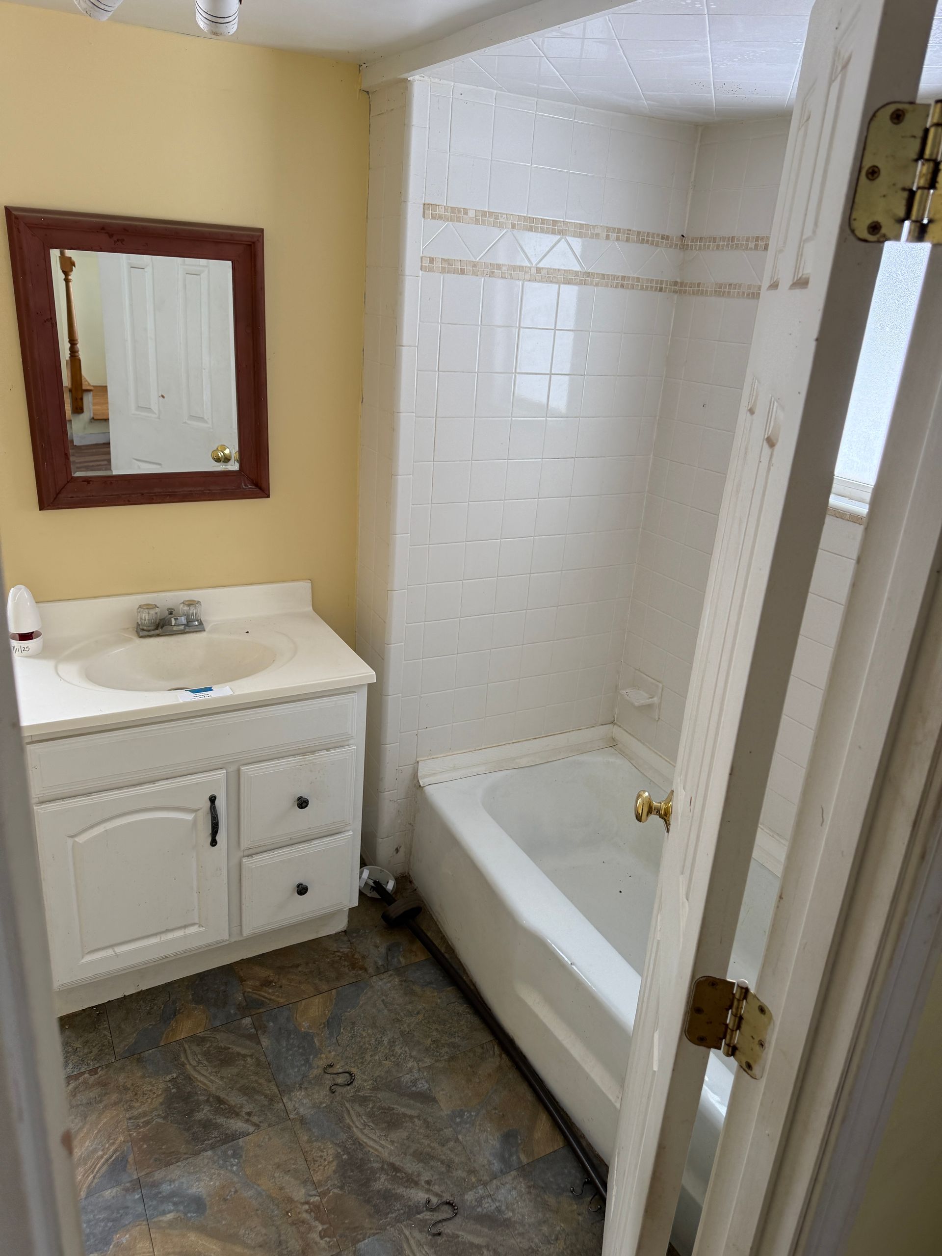Bathroom with white vanity, bathtub, and mirror; off-white and light brown walls.