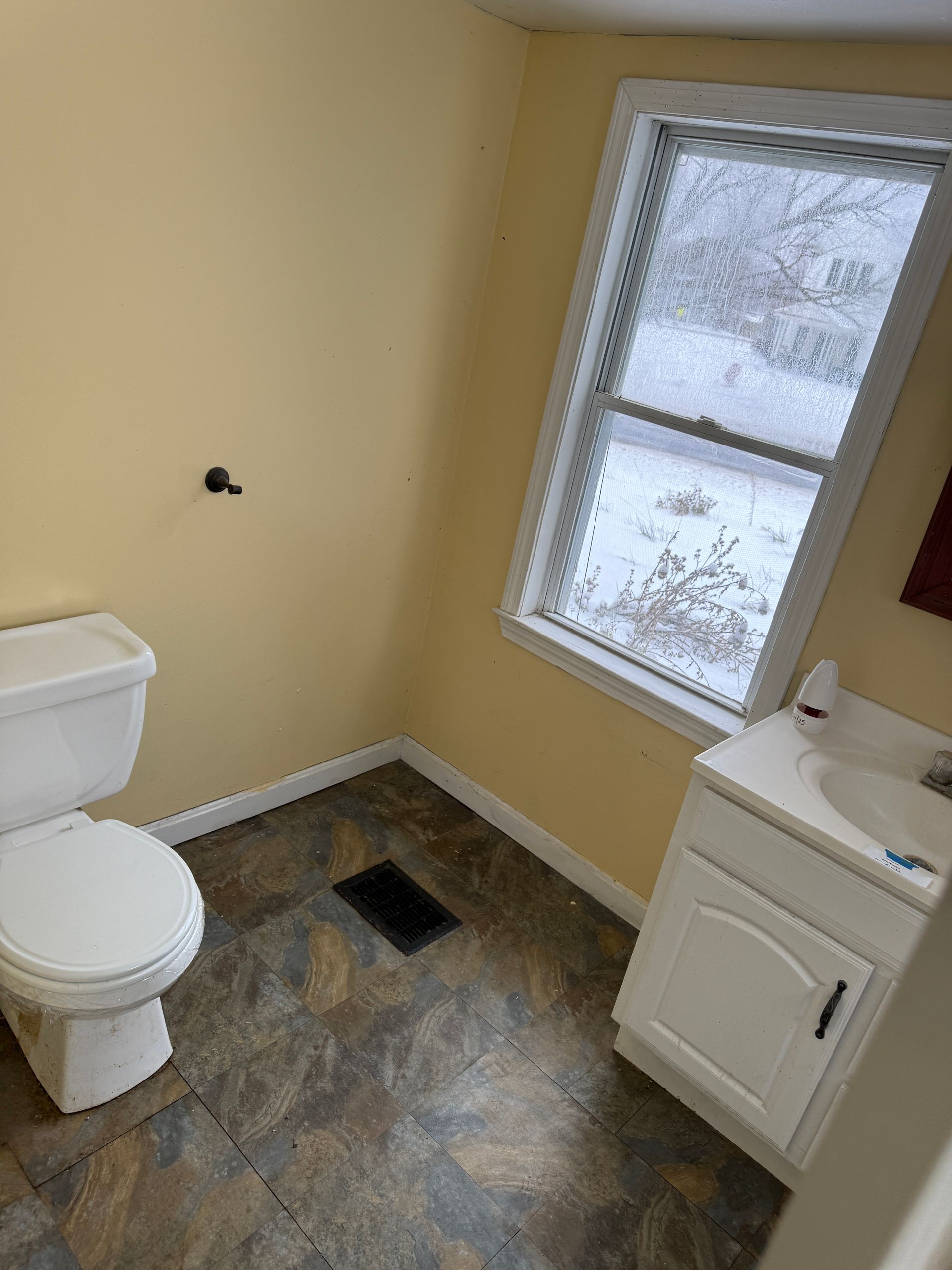 Bathroom with toilet, vanity, and window. Yellow walls, brown flooring.