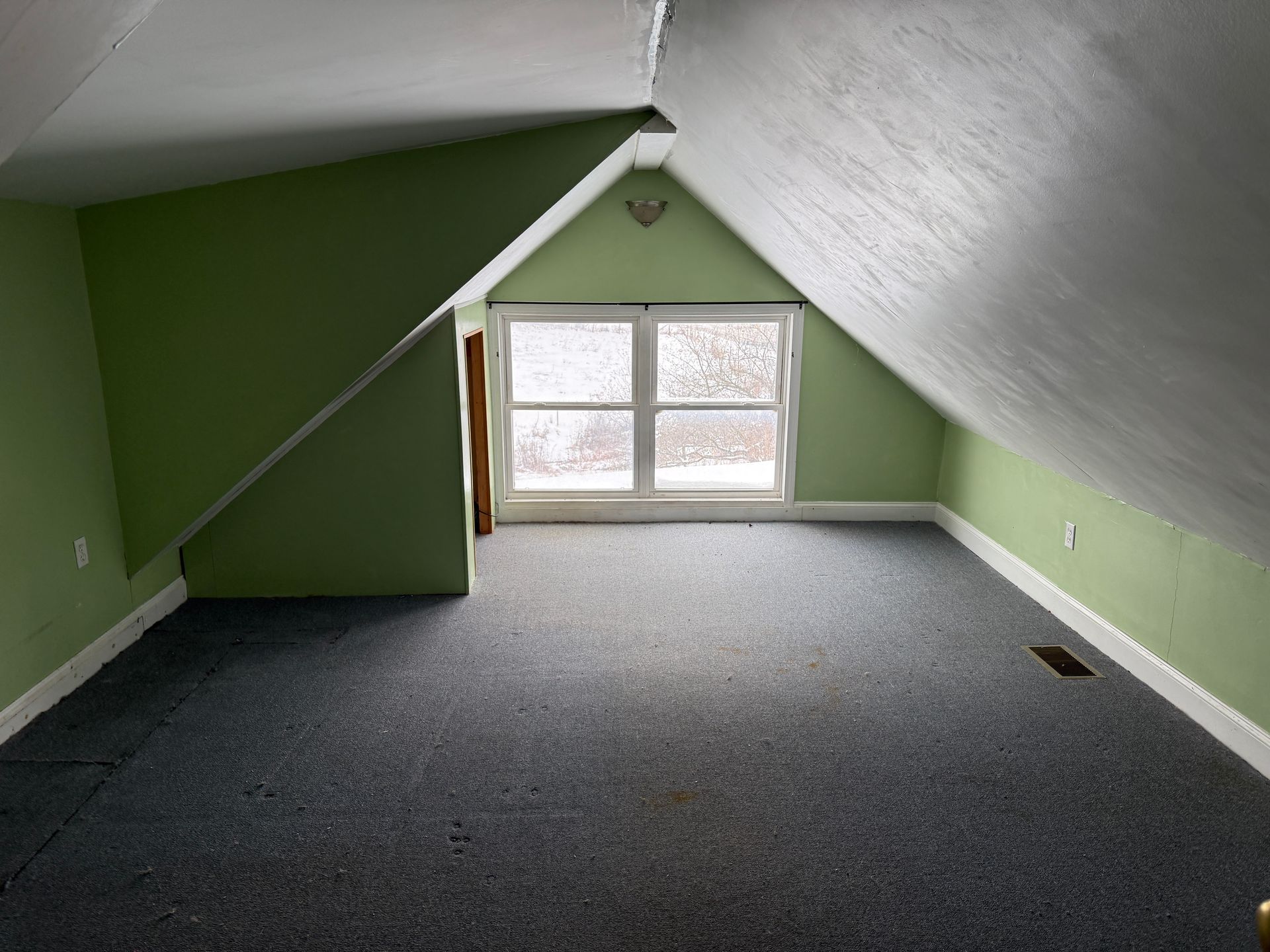 Attic room with sloped green walls, white ceiling, window, and gray carpet.