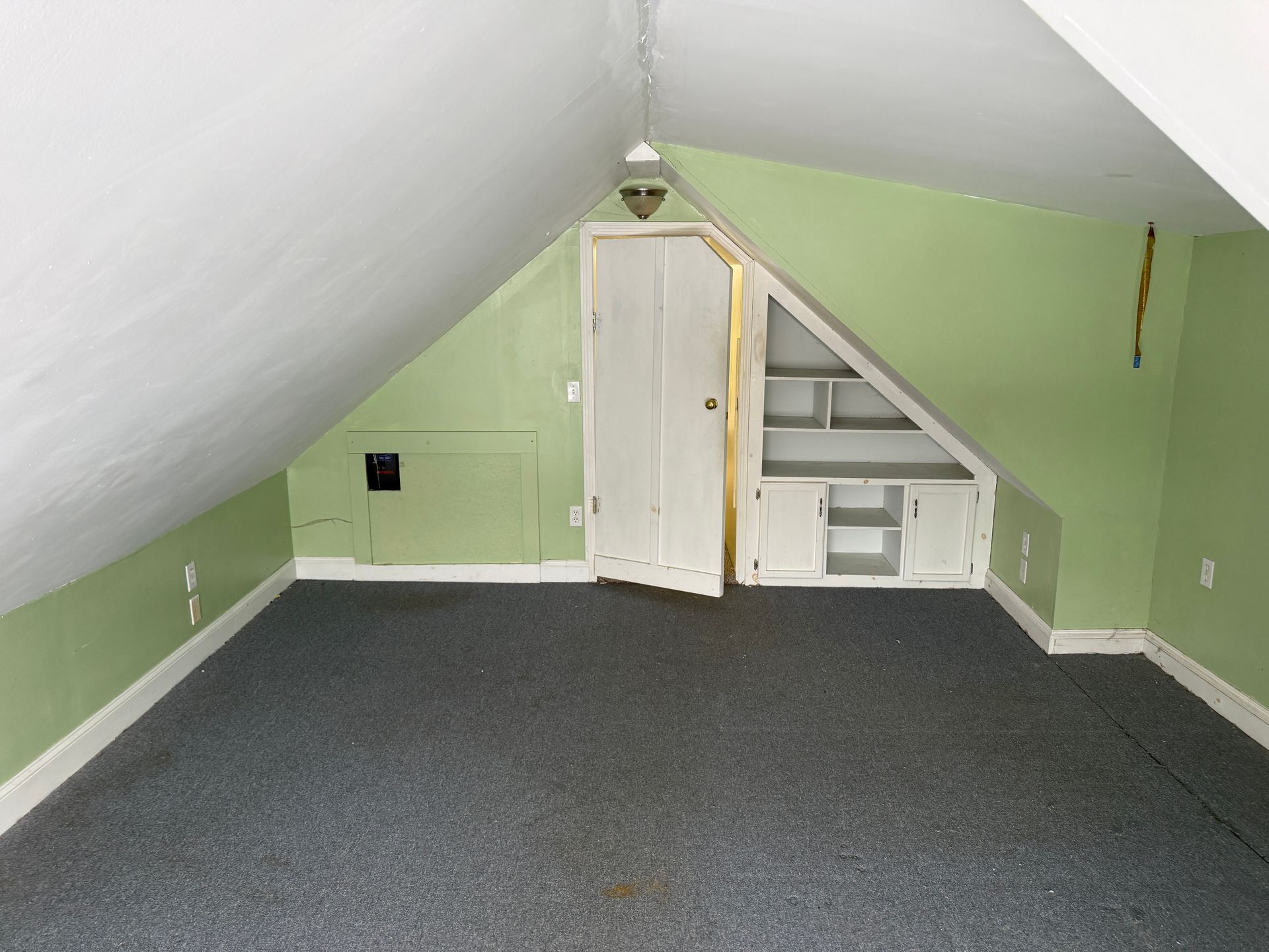 Attic room with sloped ceiling, green walls, white built-in storage, gray carpet, and a central light fixture.