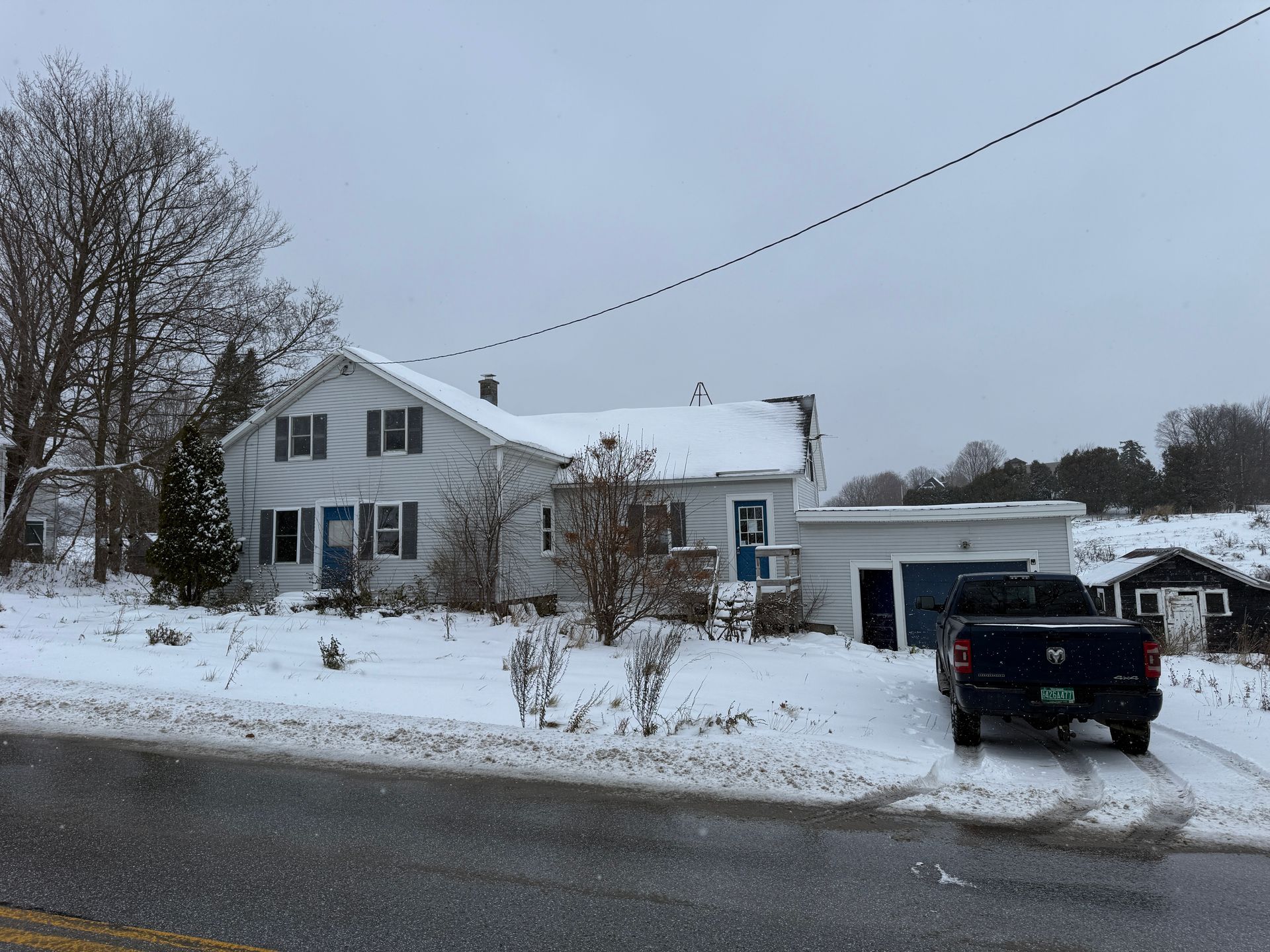 Snow-covered house with a truck parked in the driveway; overcast sky.