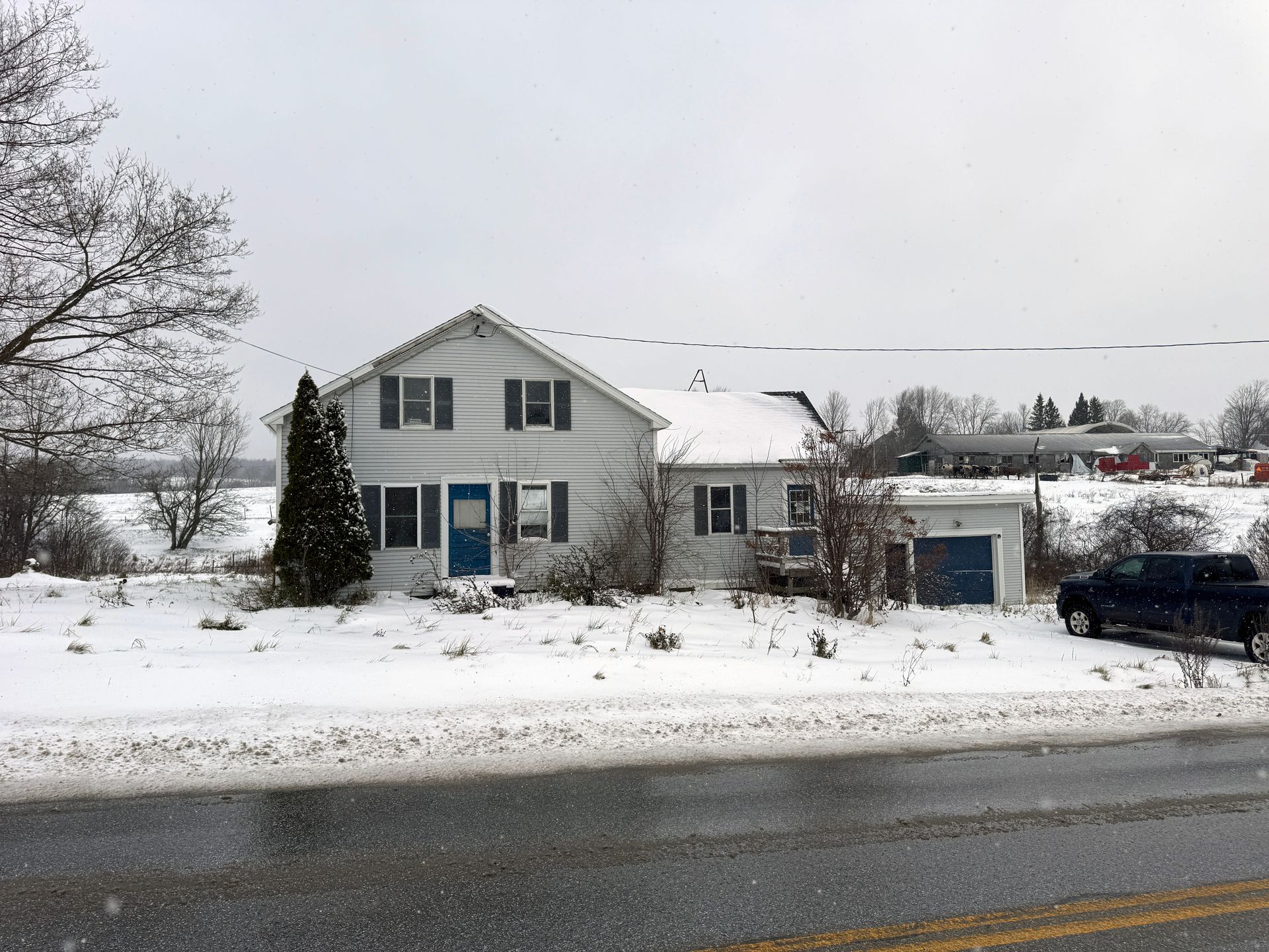 Two-story white house with blue door and attached garage, snow on the ground, overcast day.