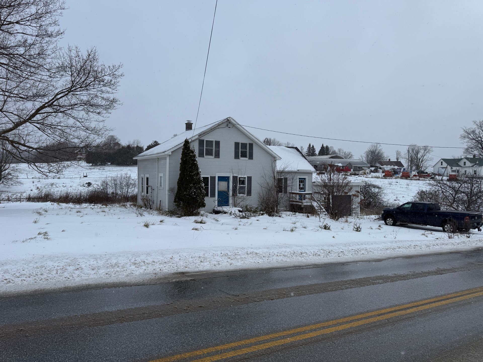White house with black shutters, snow-covered yard, blue front door, overcast day.