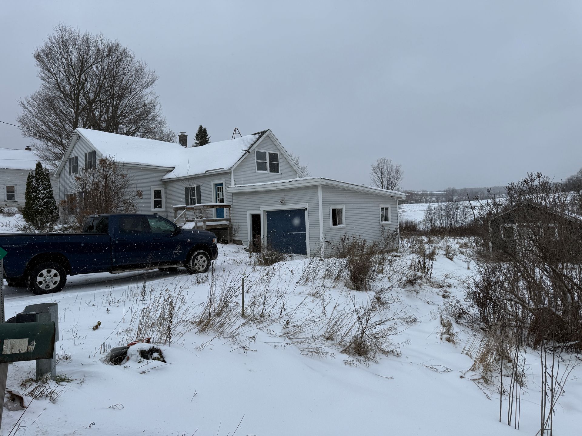 Snowy scene: white house with attached garage, blue pickup truck in driveway, field in the background.