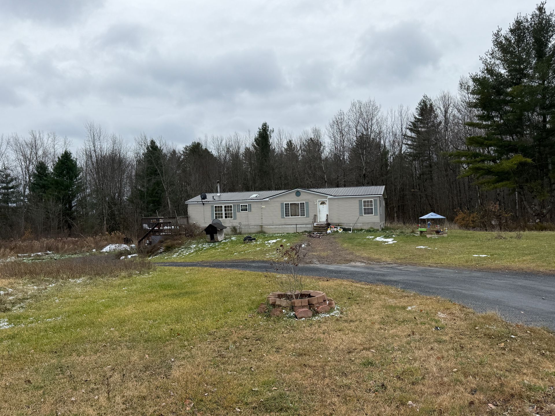 Mobile home on a gravel driveway in a rural wooded area under a cloudy sky