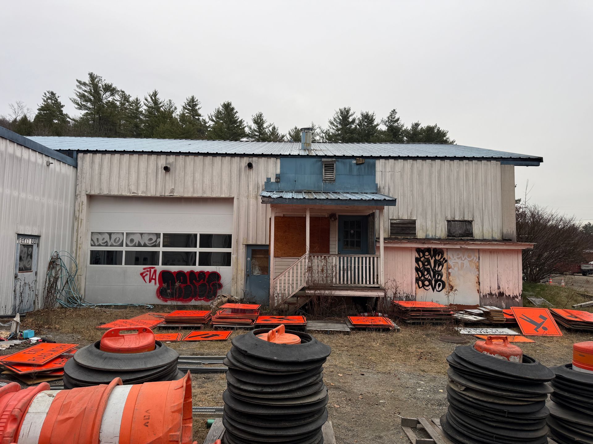 Building with a garage door, a porch, and stacked orange traffic cones.