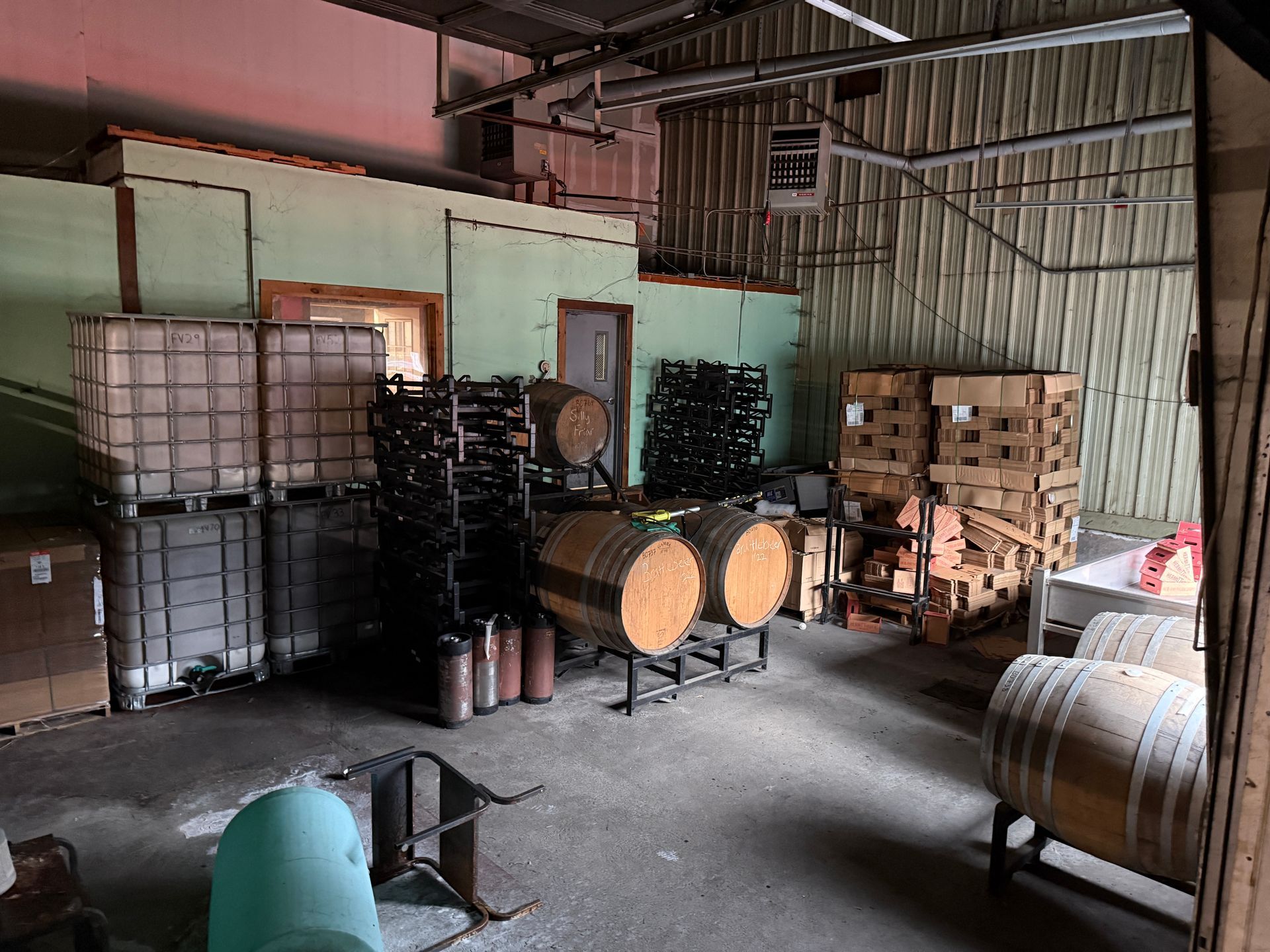 Interior of a storage area: barrels, stacked boxes, tanks, and racks.