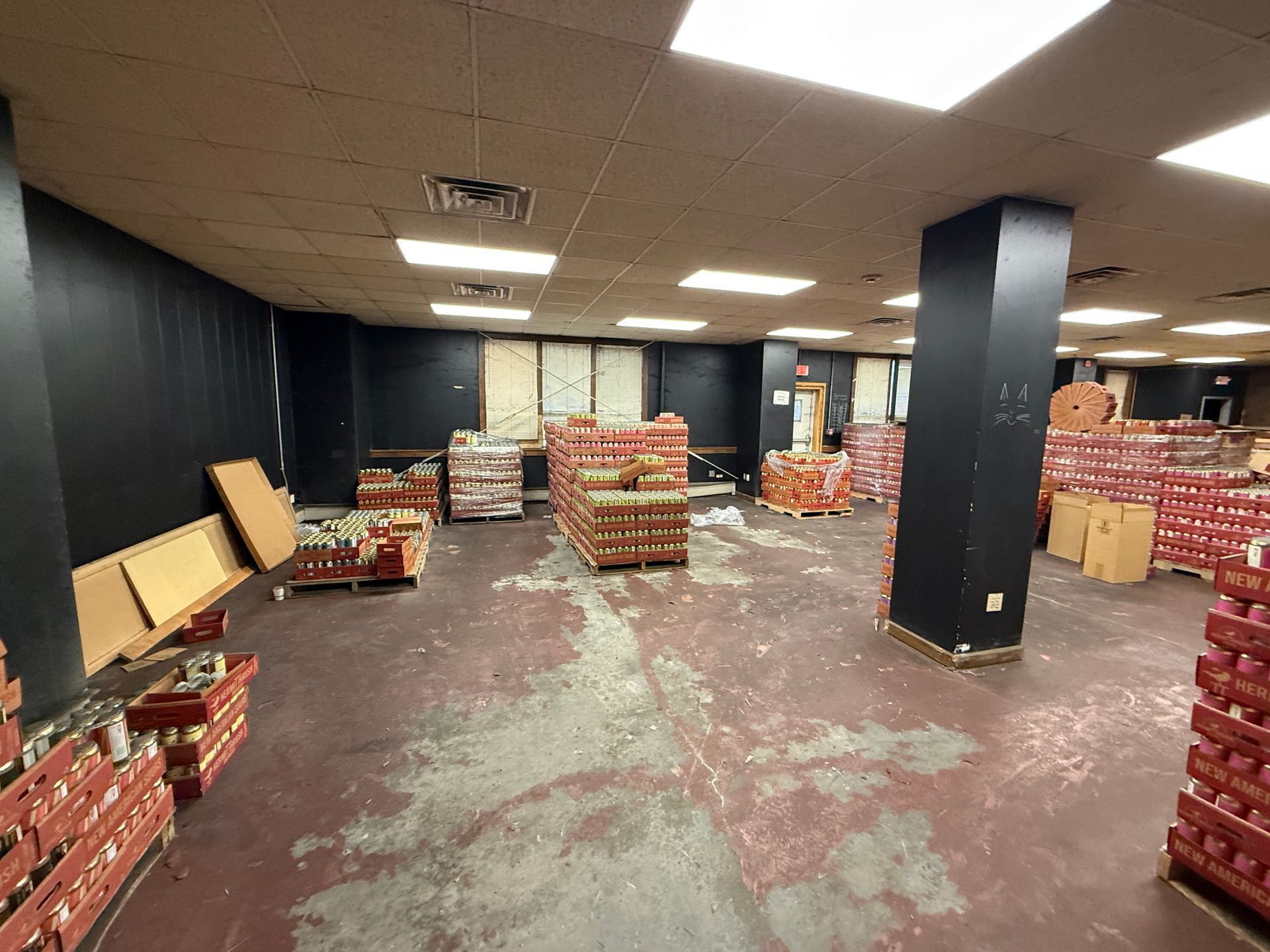 Warehouse with pallets of red produce, black columns and walls, concrete floor and fluorescent lights.
