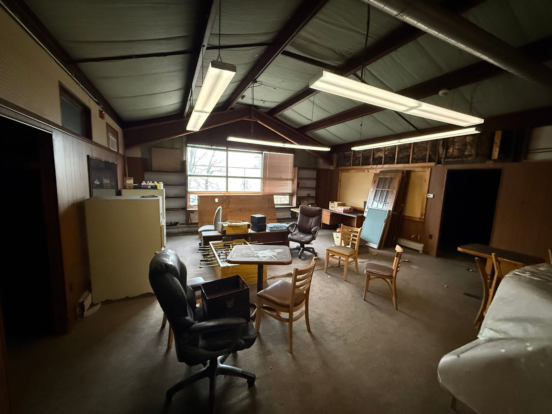 Interior shot of an office space. Desks and chairs are scattered throughout the room, under fluorescent lights.