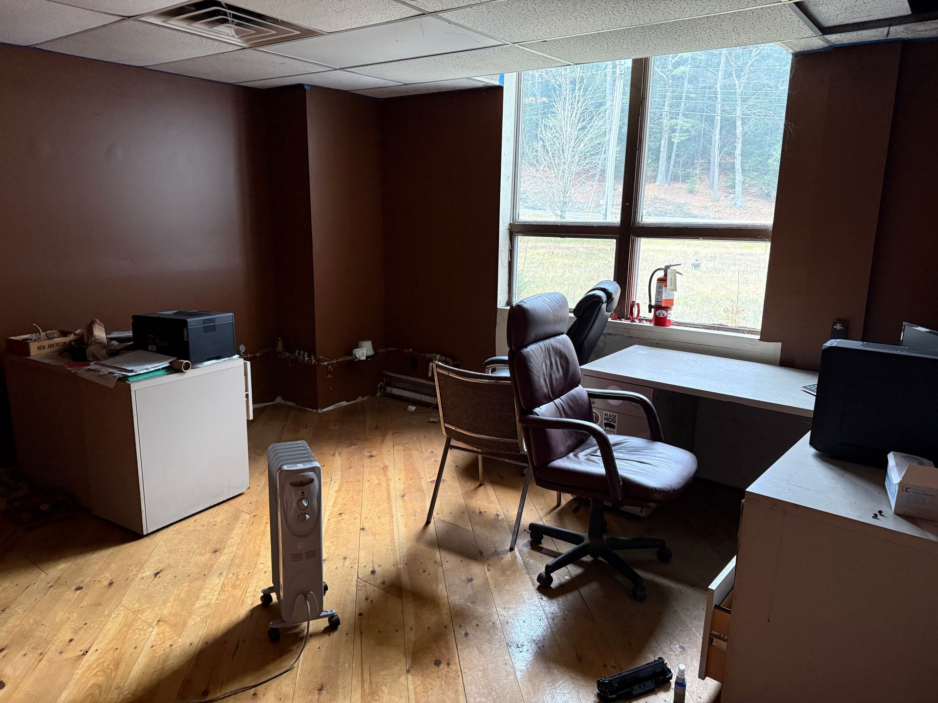 Office interior with wood floors, brown walls, desk, chairs, and window overlooking trees.