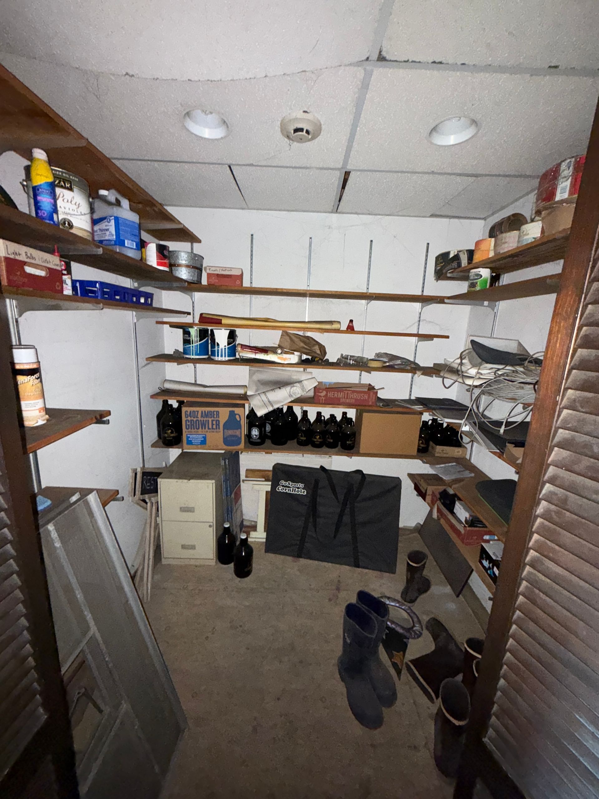 A storage room with shelves filled with items, including containers, boxes, and tools; concrete floor.
