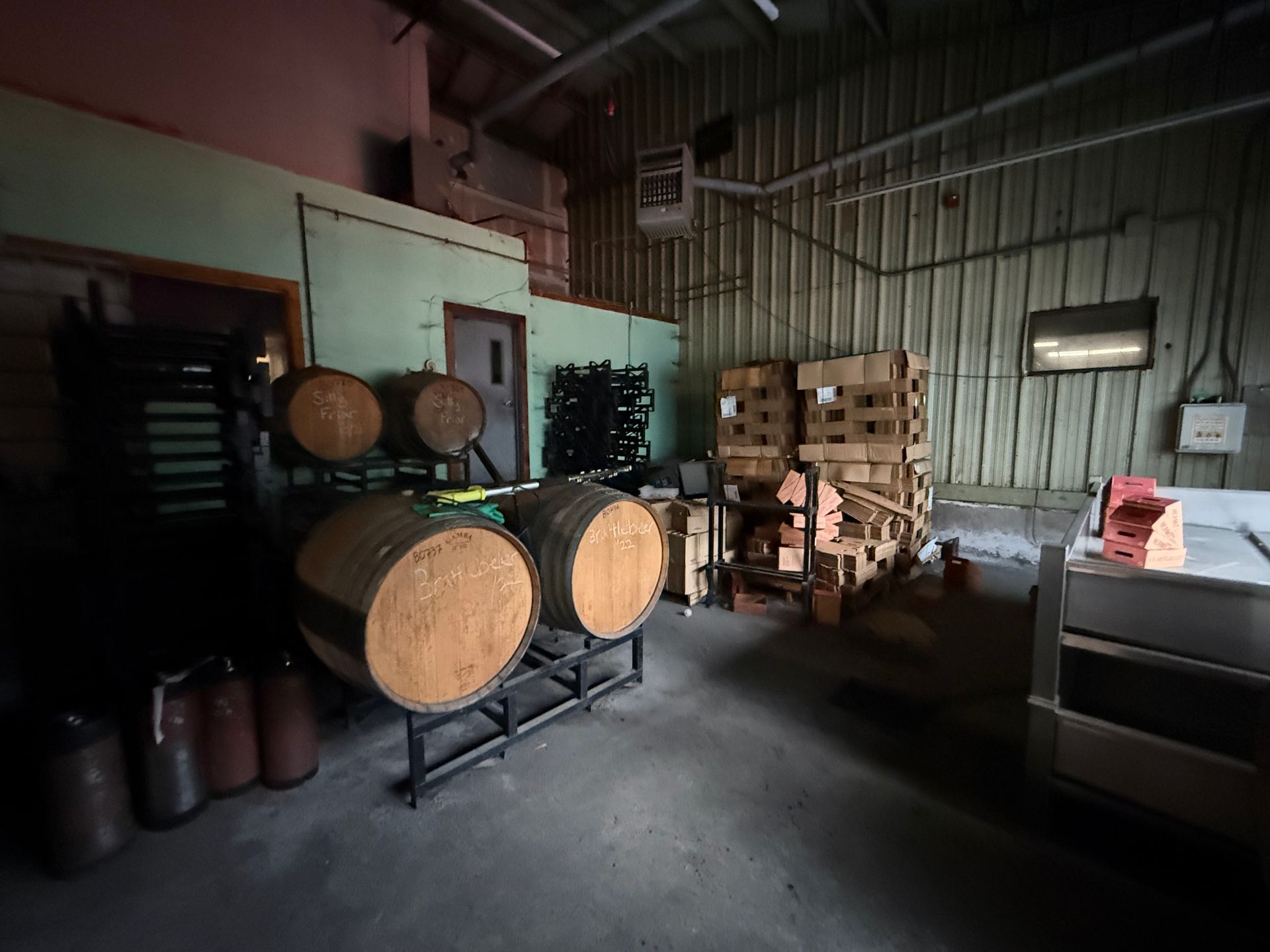 Interior of a warehouse with barrels, stacked boxes, and equipment.
