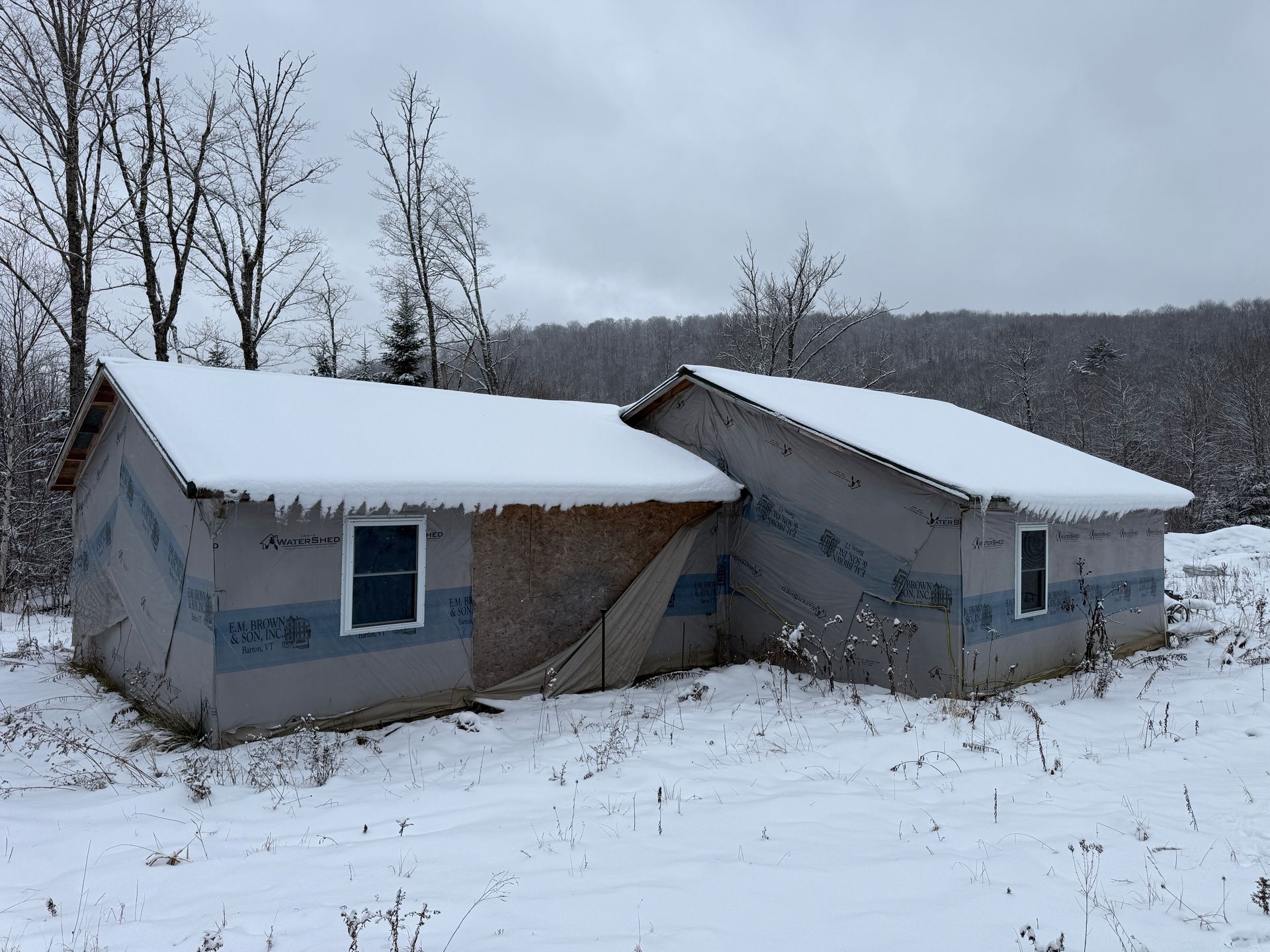 A snow-covered building with two connected sections in a snowy, wooded area.