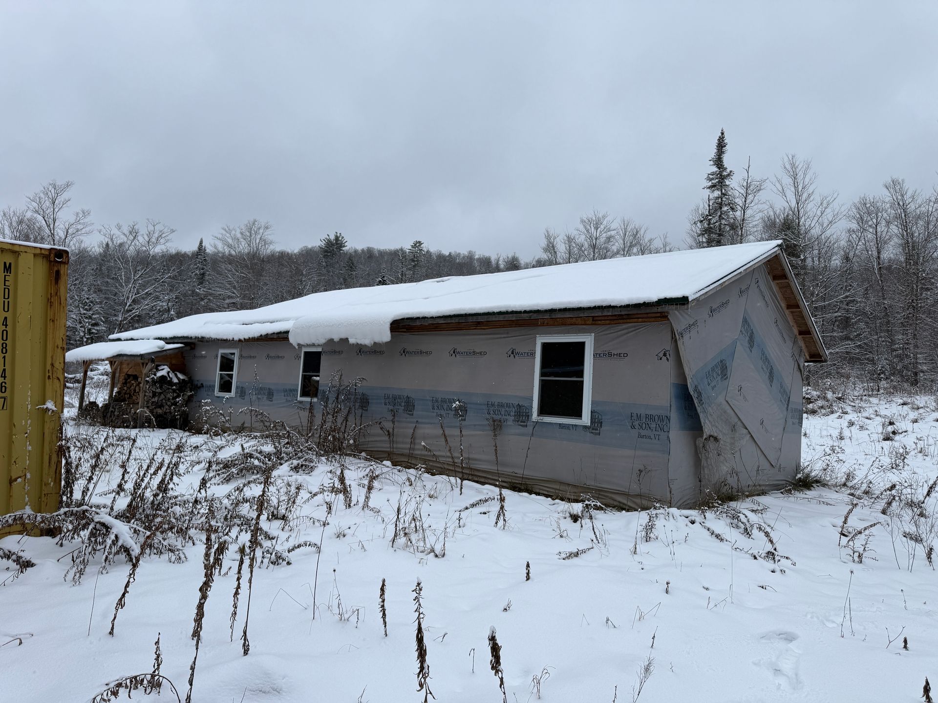 Single-story building under construction, snow-covered roof, windows, and surrounding field of snow.
