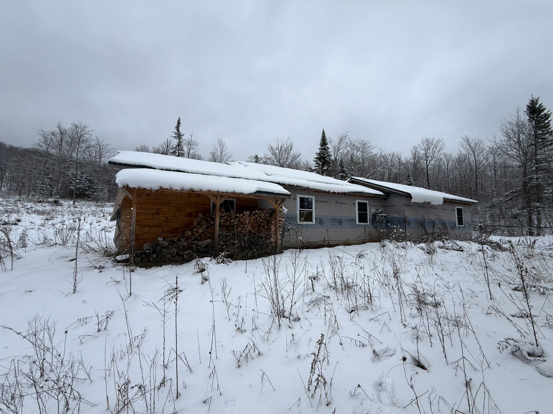 Snow-covered cabin in a field, under a cloudy sky.