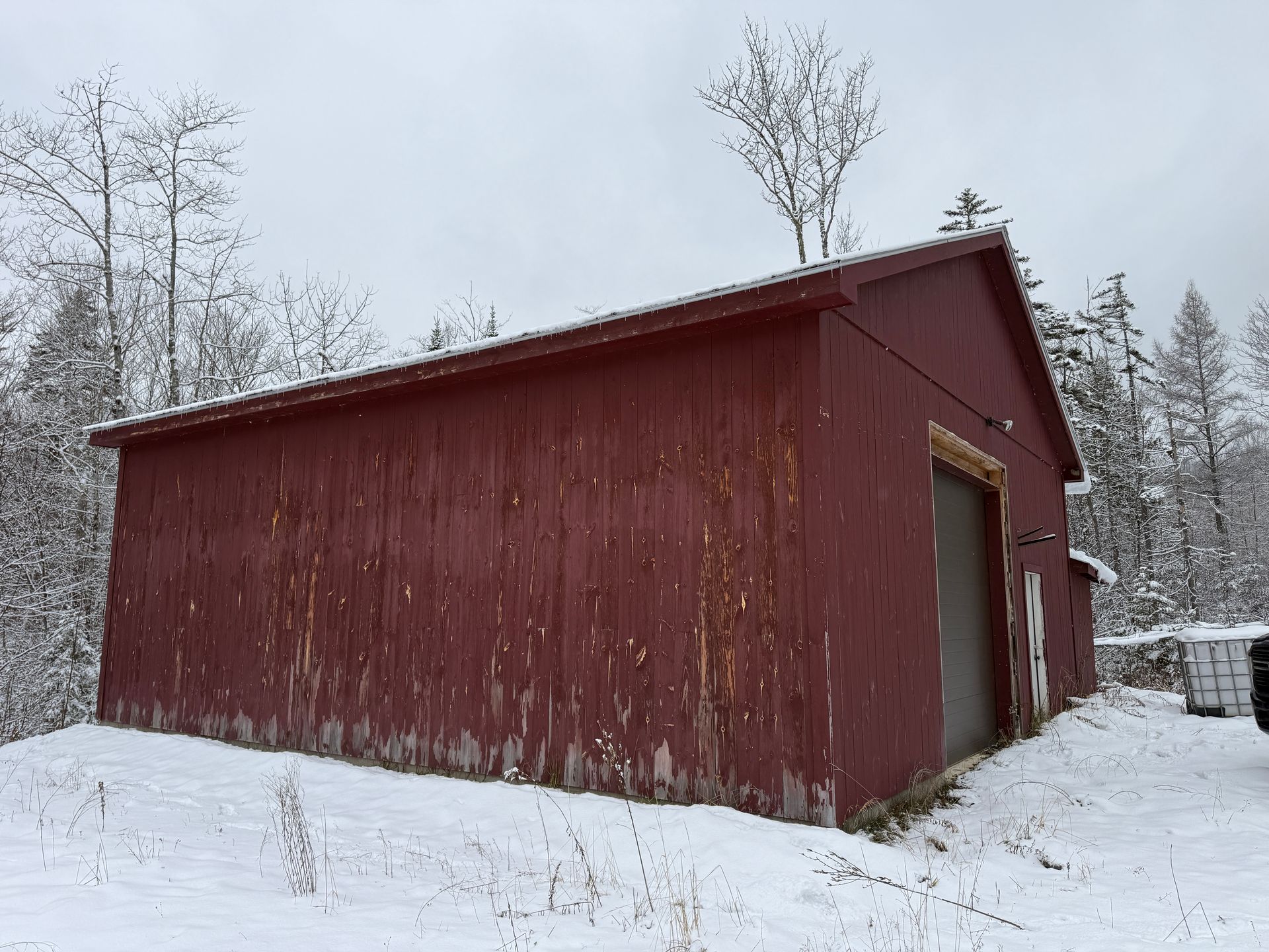 Red wooden shed in a snowy landscape. Trees in the background, overcast sky.