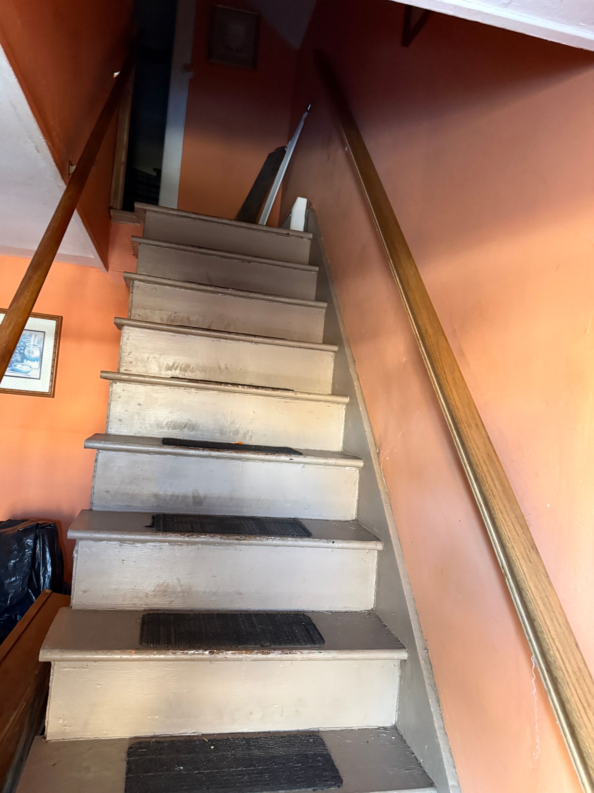 Staircase with worn, gray steps and wooden handrails ascending between orange walls.