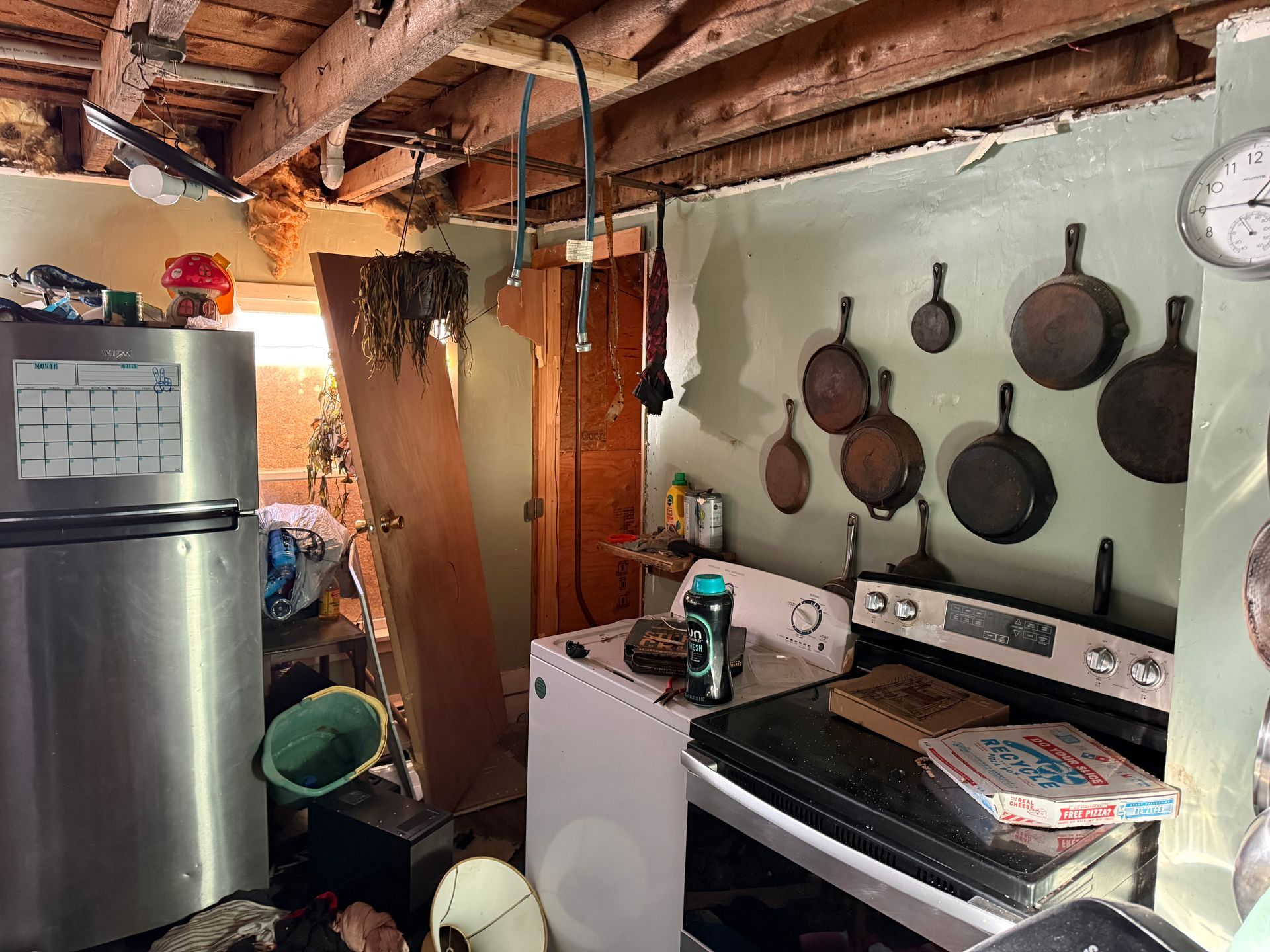 Rustic kitchen with exposed ceiling beams, stainless steel fridge, stove, and cast iron pans on wall.