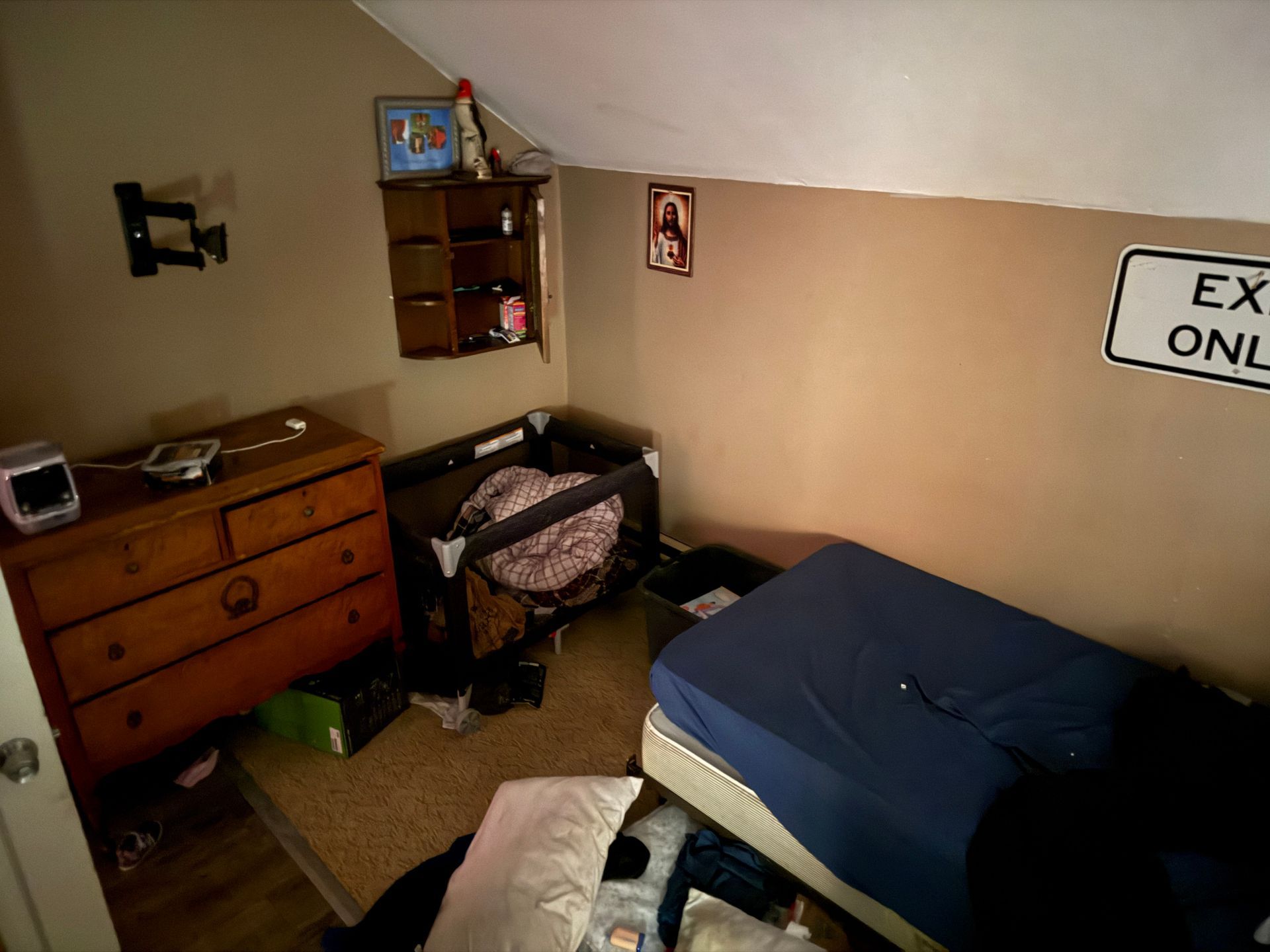 Bedroom with a bed, dresser, crib, and exit only sign on the wall.