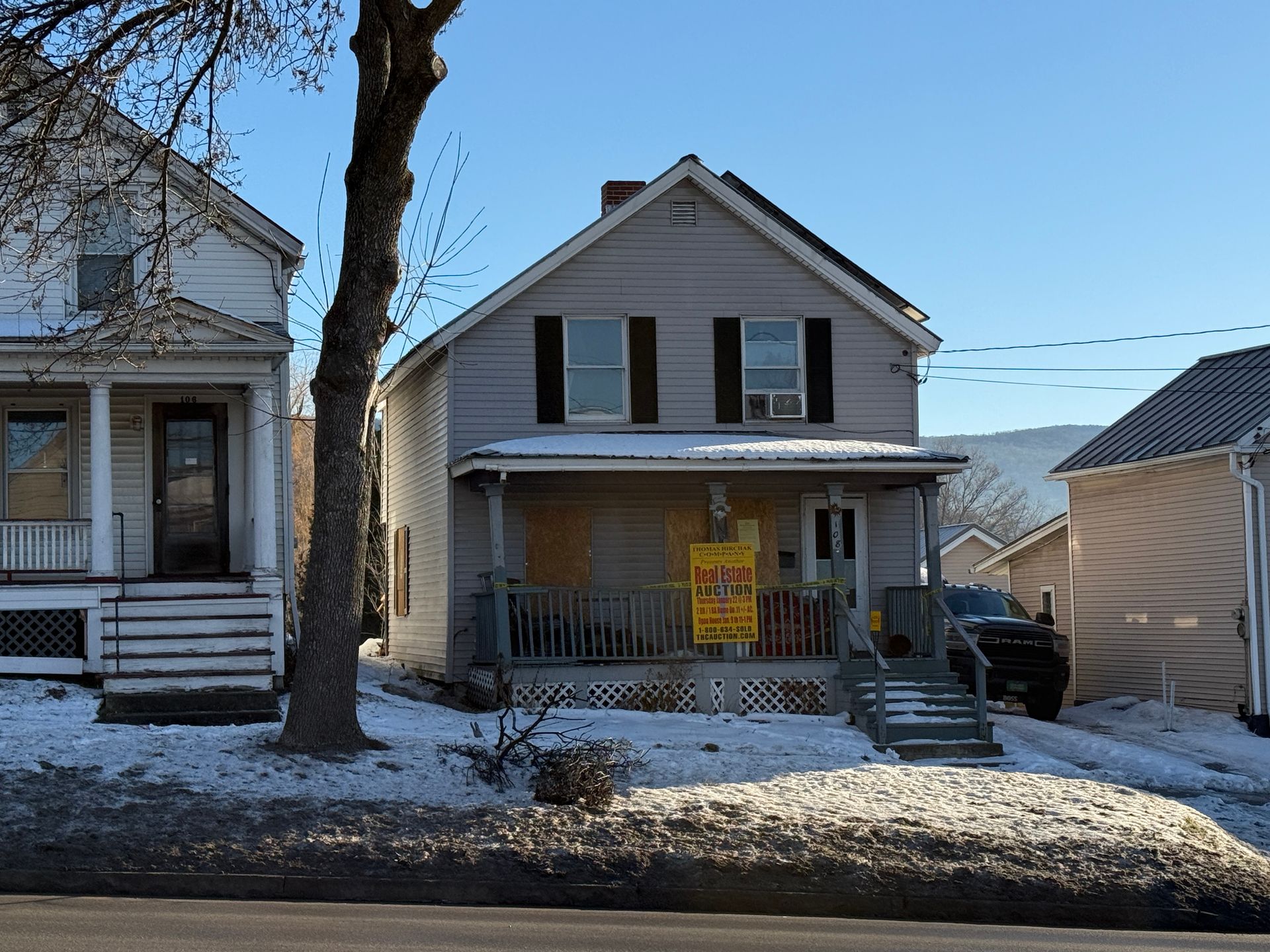 Two-story house with porch, snow-covered ground, and a clear blue sky.