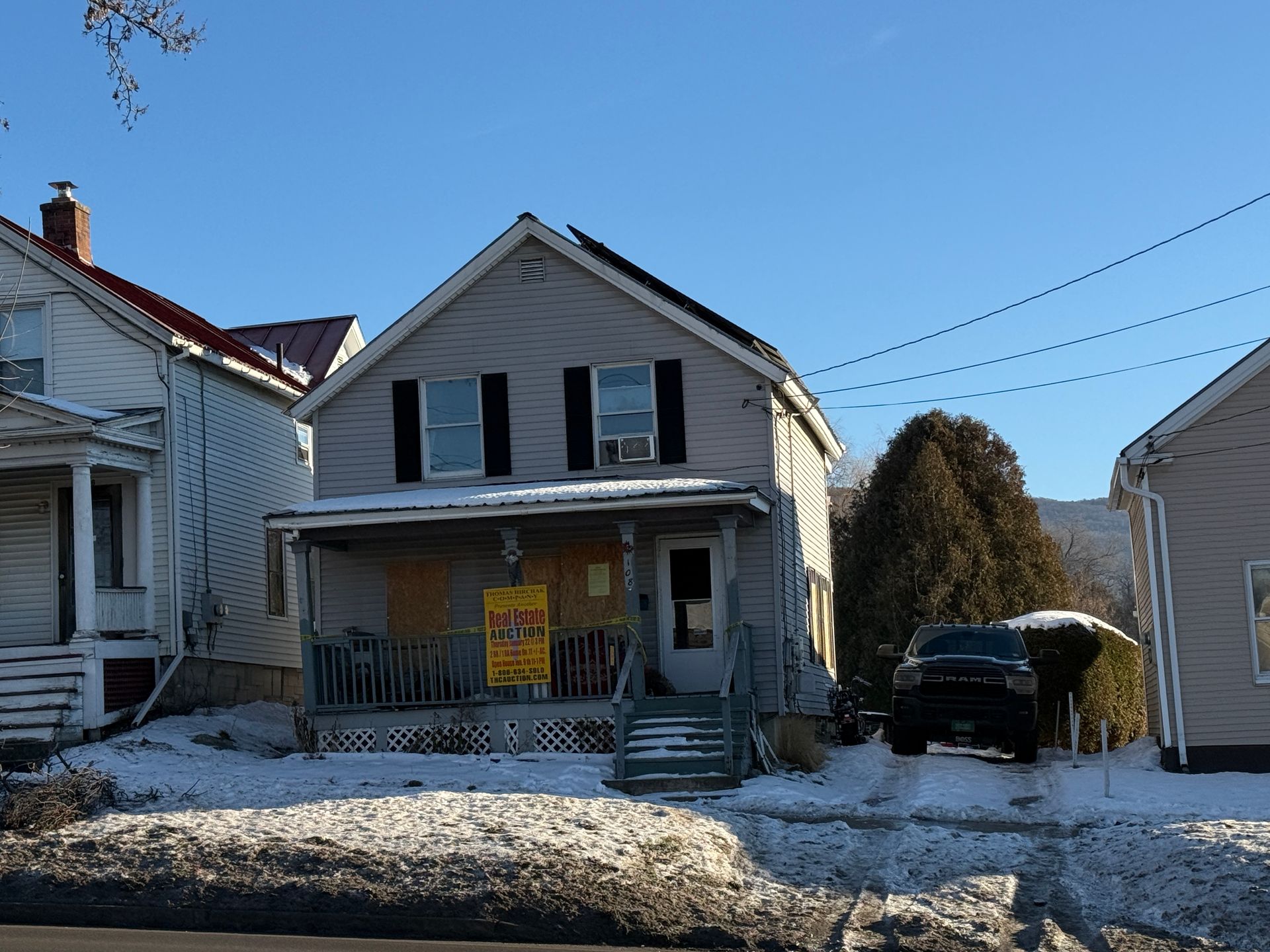 Two-story gray house with black shutters, snow on the ground, and a vehicle parked on the side.