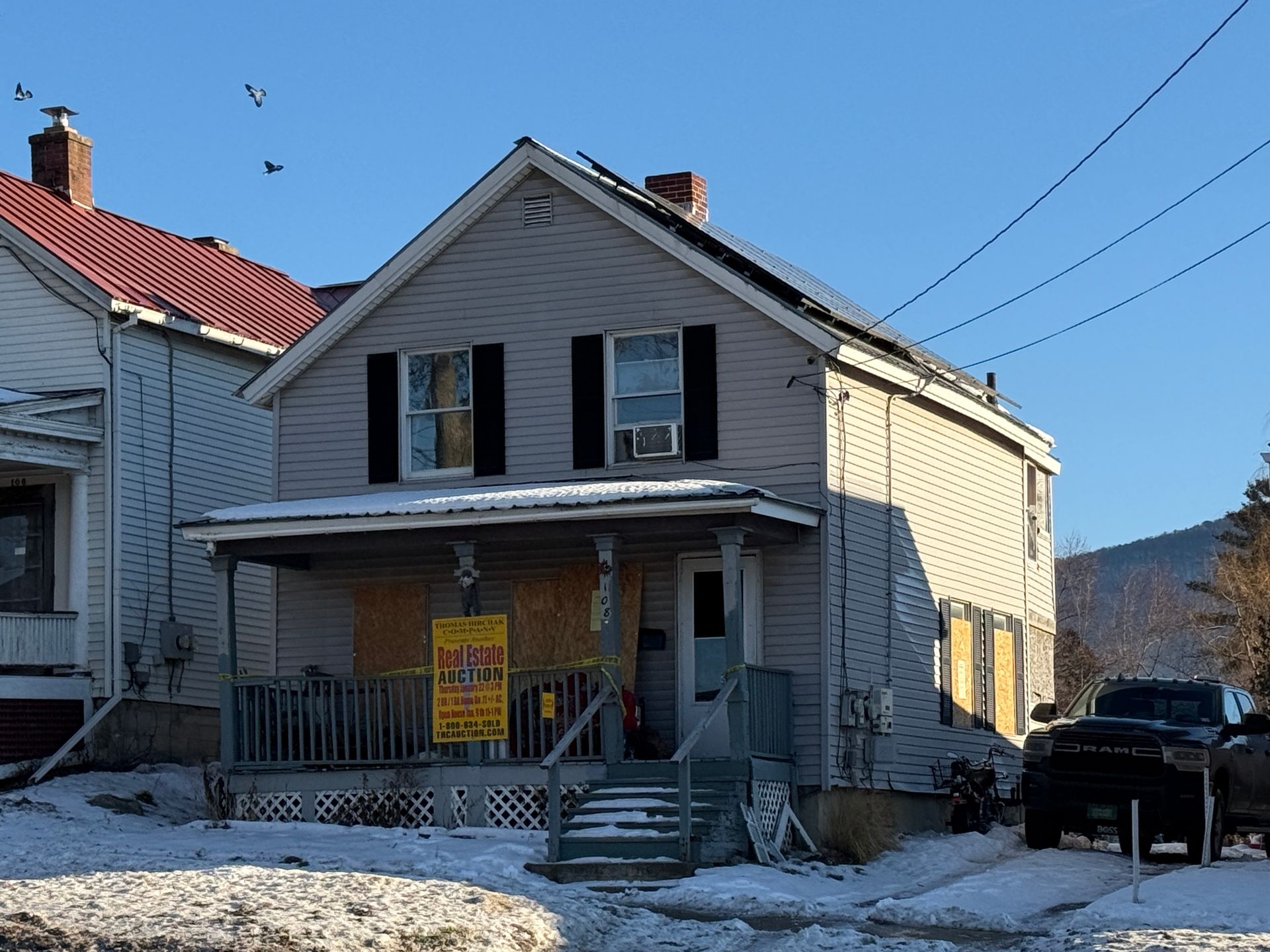 Two-story house with a porch and solar panels on the roof; snow on the ground; parked truck.