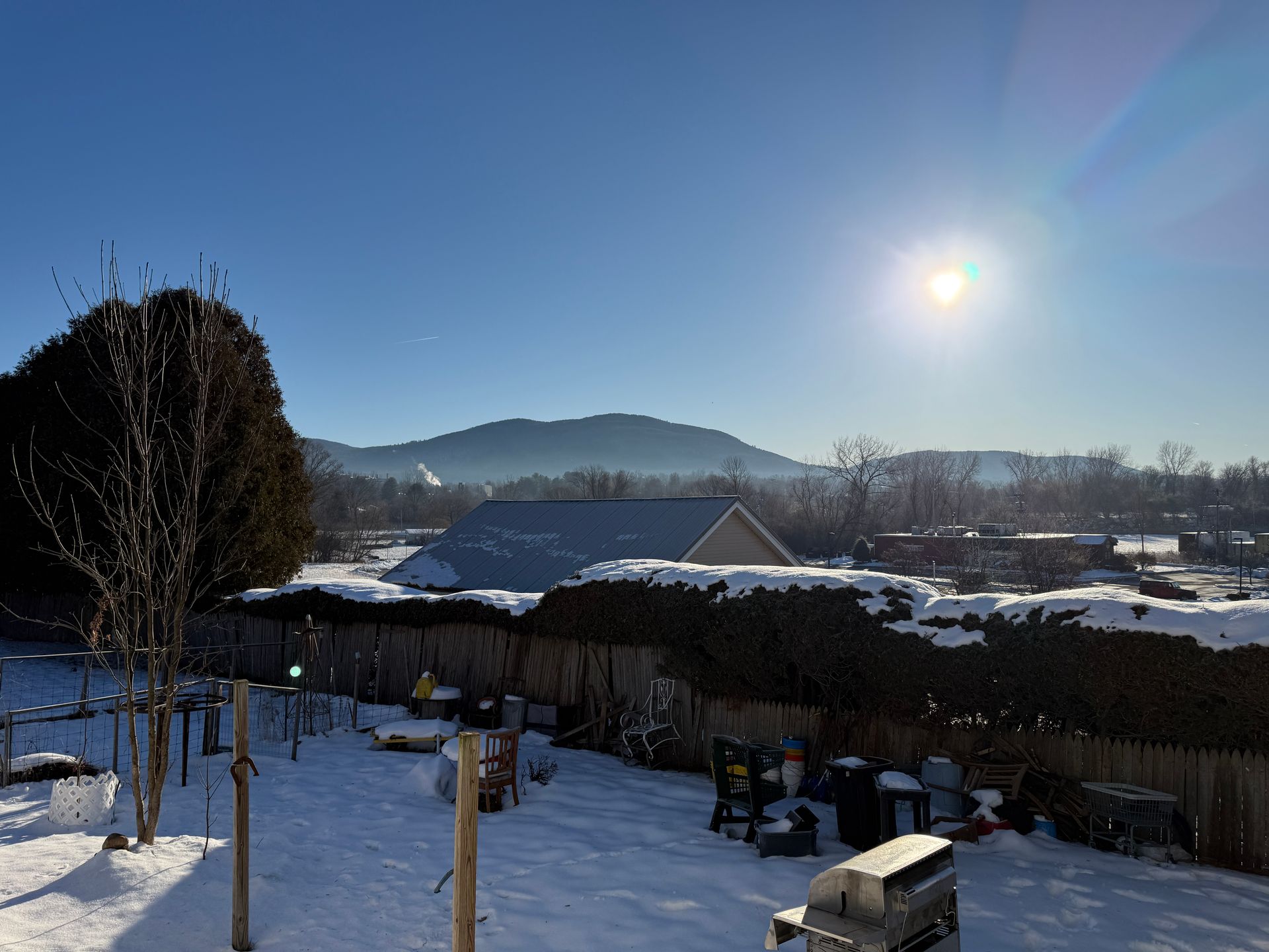 Snowy backyard scene with sunlit mountain and blue sky.