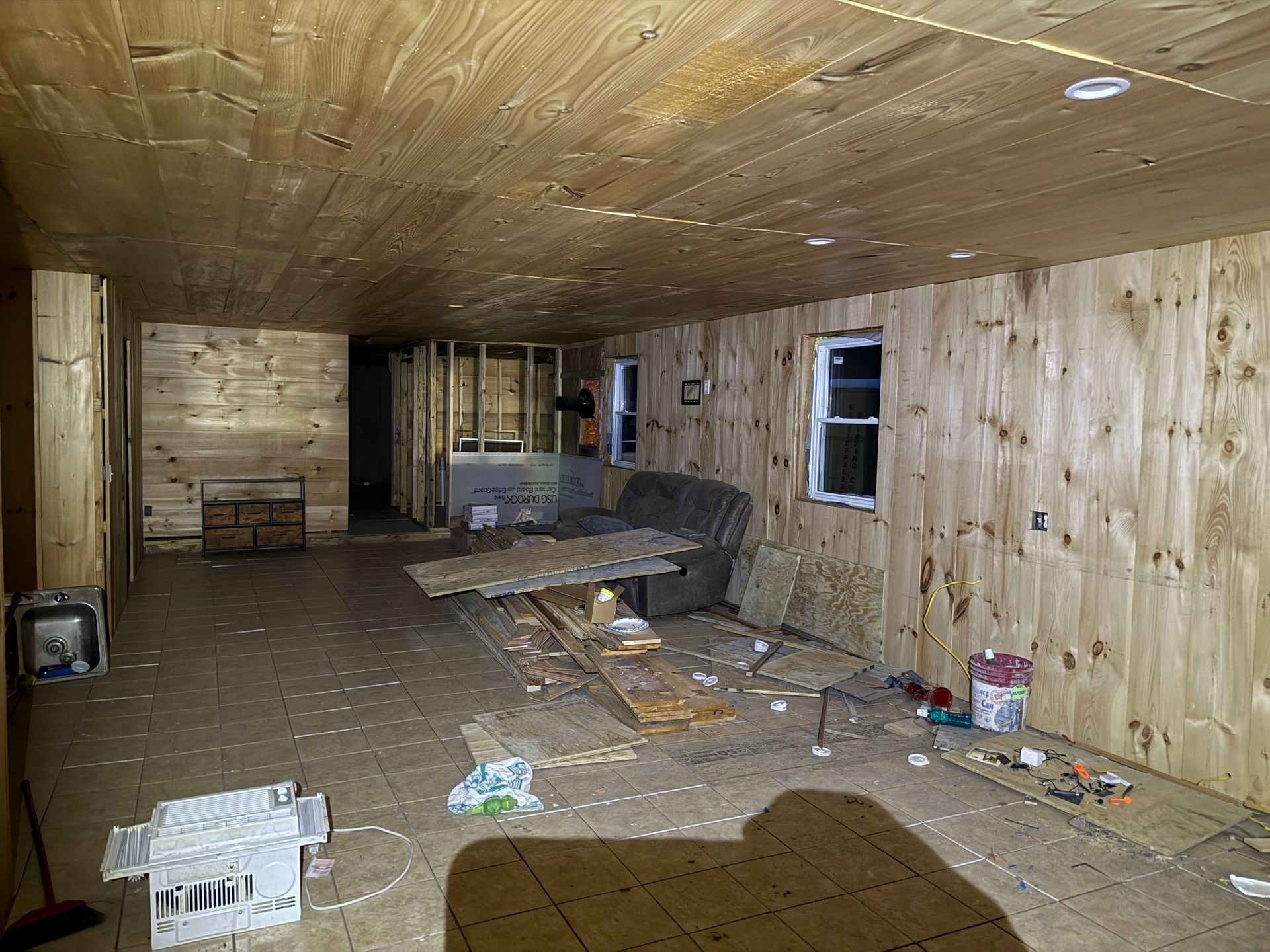 Interior of a room with wood walls and ceiling, containing furniture and construction items.