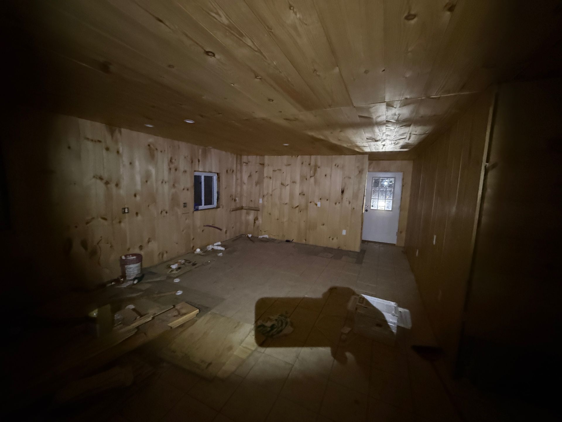 Interior of a room with wood paneling. A small window and a door are visible.
