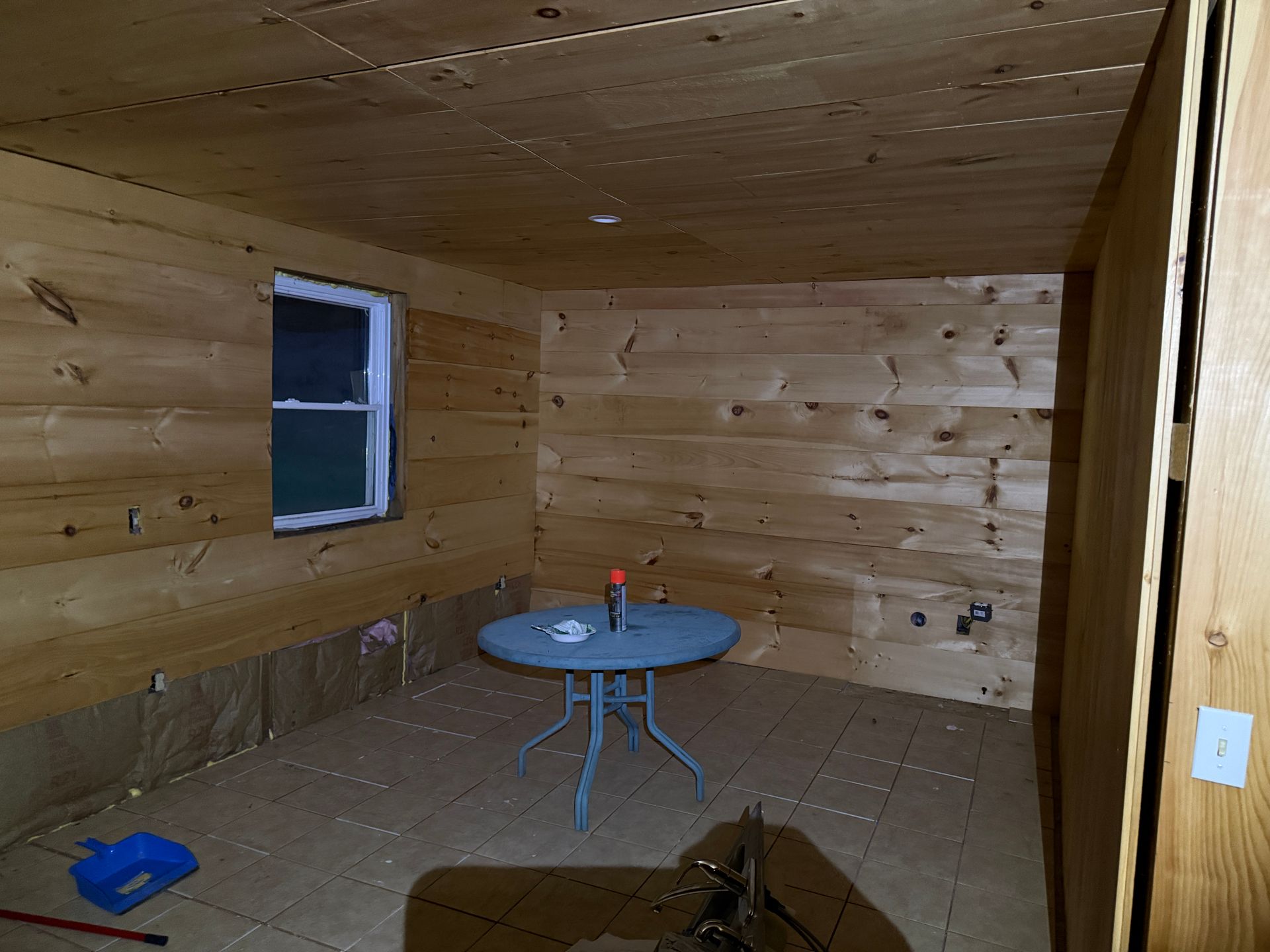 Interior of a room with wood paneling, a small round table, window, and a door opening.