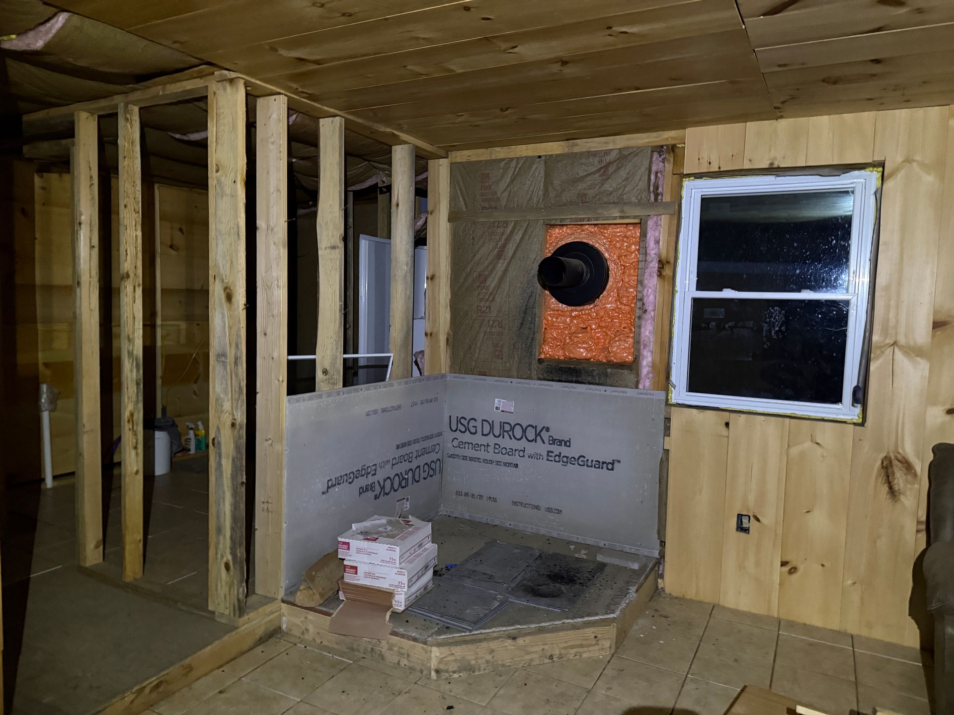 Interior room under construction, with wooden frame, drywall, window, and unfinished shower area.