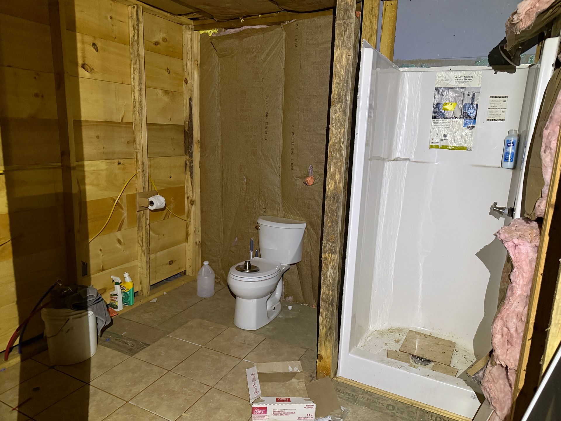 Bathroom under construction with a toilet, shower, and insulation visible. Wooden beams and walls.