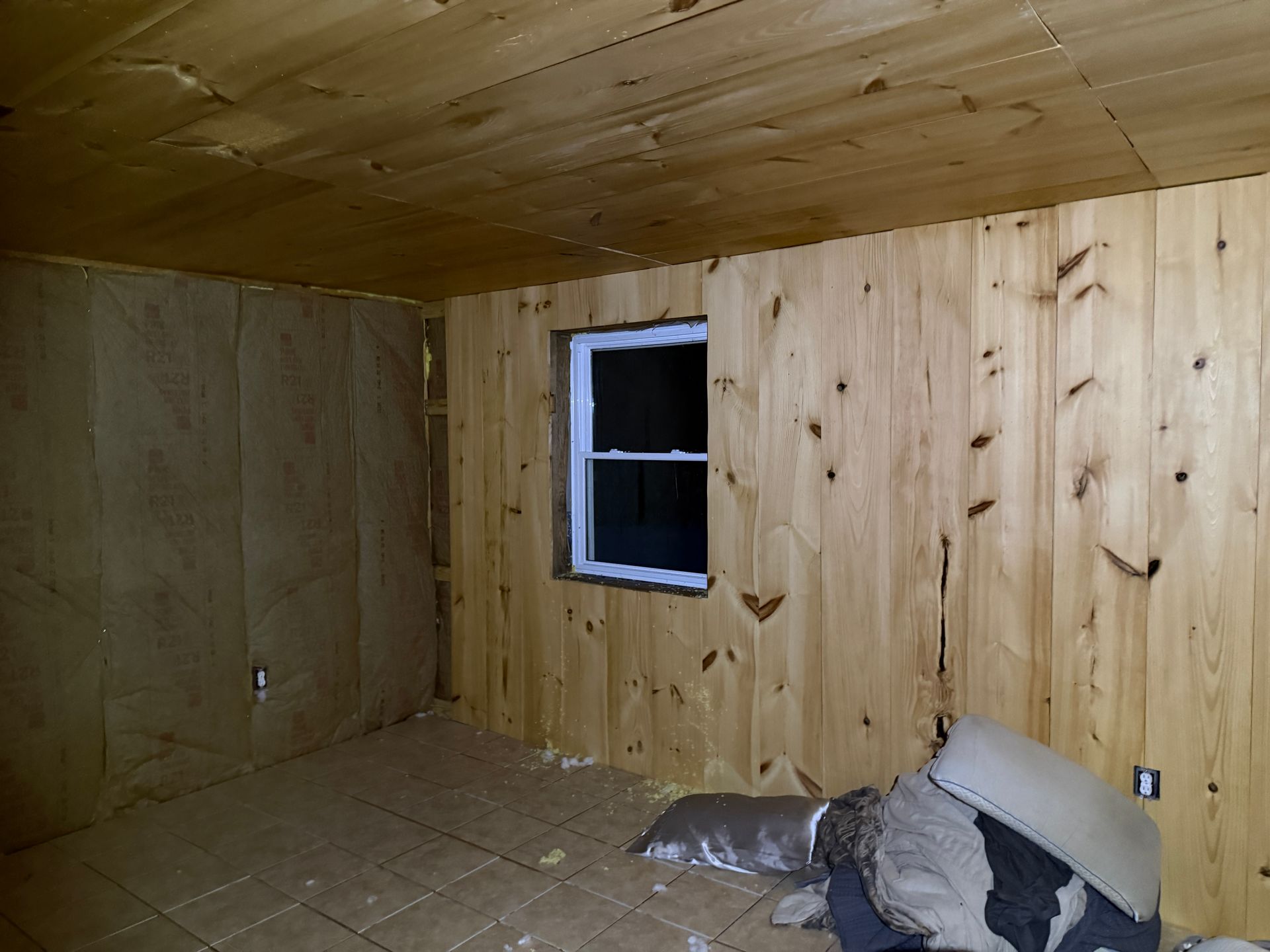 Wooden paneled room with window. Some materials on the floor.