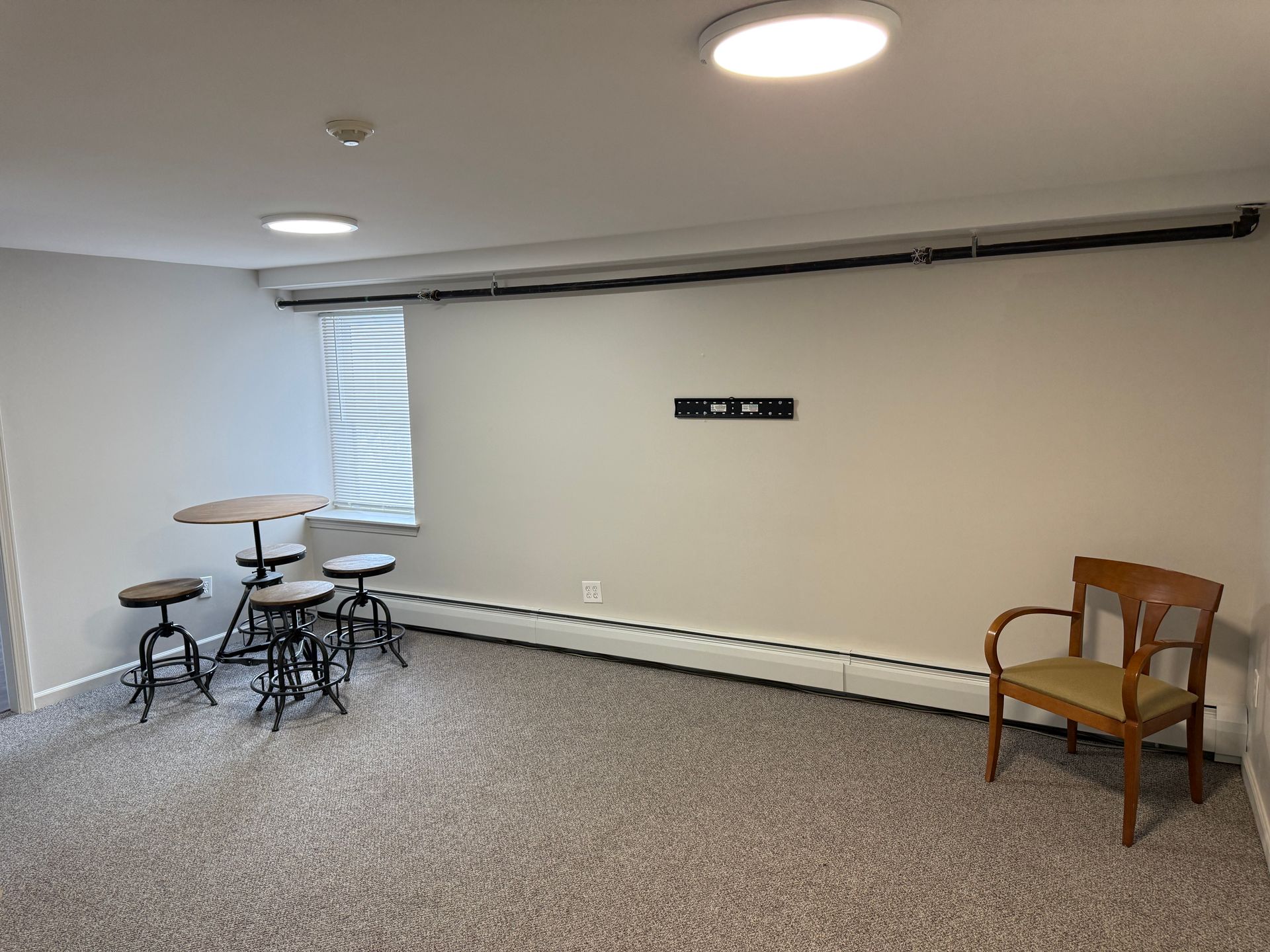 Empty room with round table and stools, a chair, and a wall-mounted TV bracket.