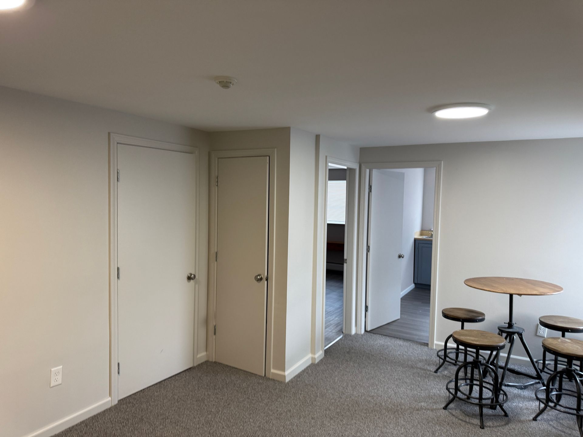 Interior view of a room with two doors, carpet flooring, and a small table with stools.