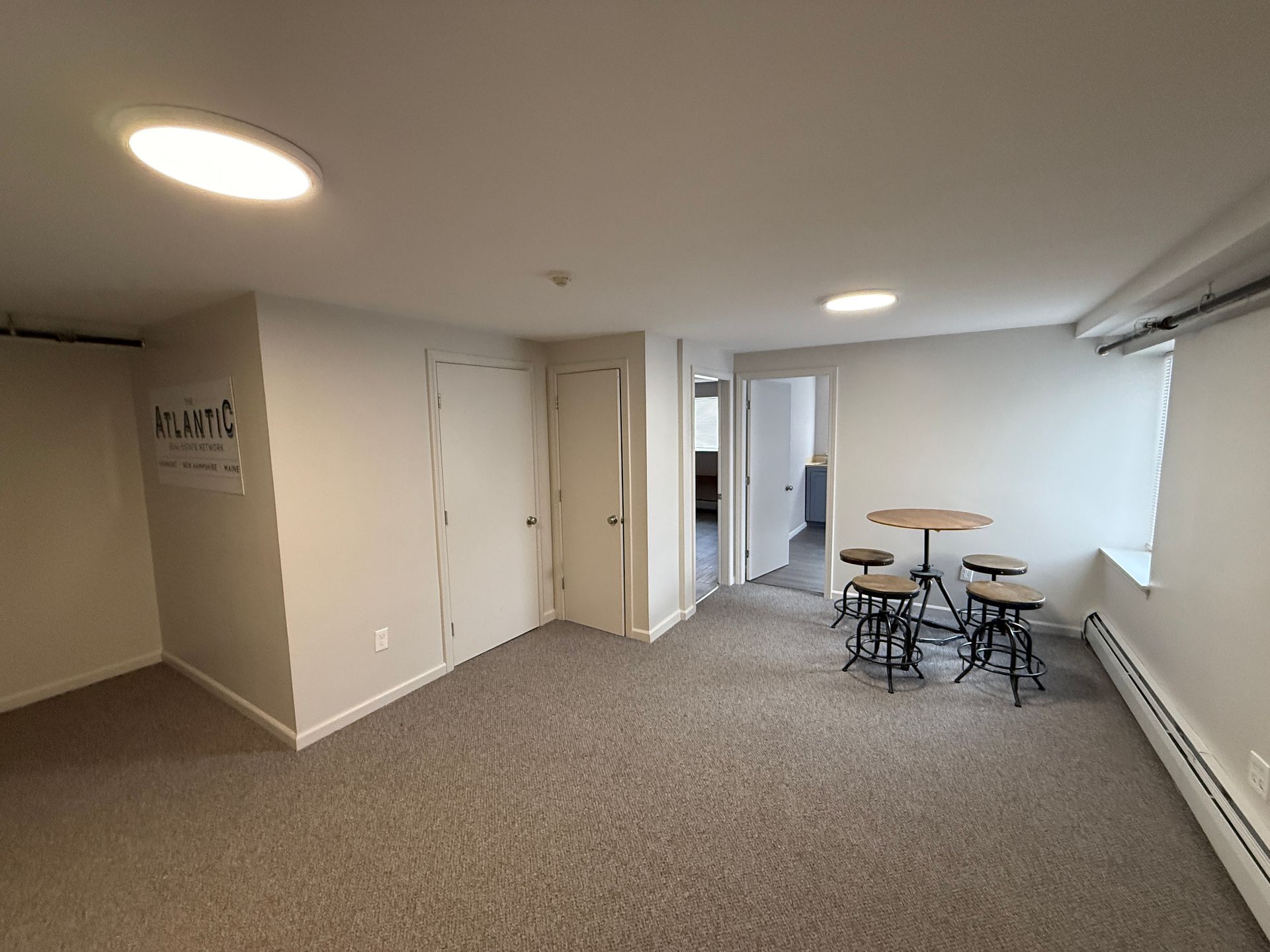 Empty room with carpet, two doors, a small table with stools, and overhead lighting.