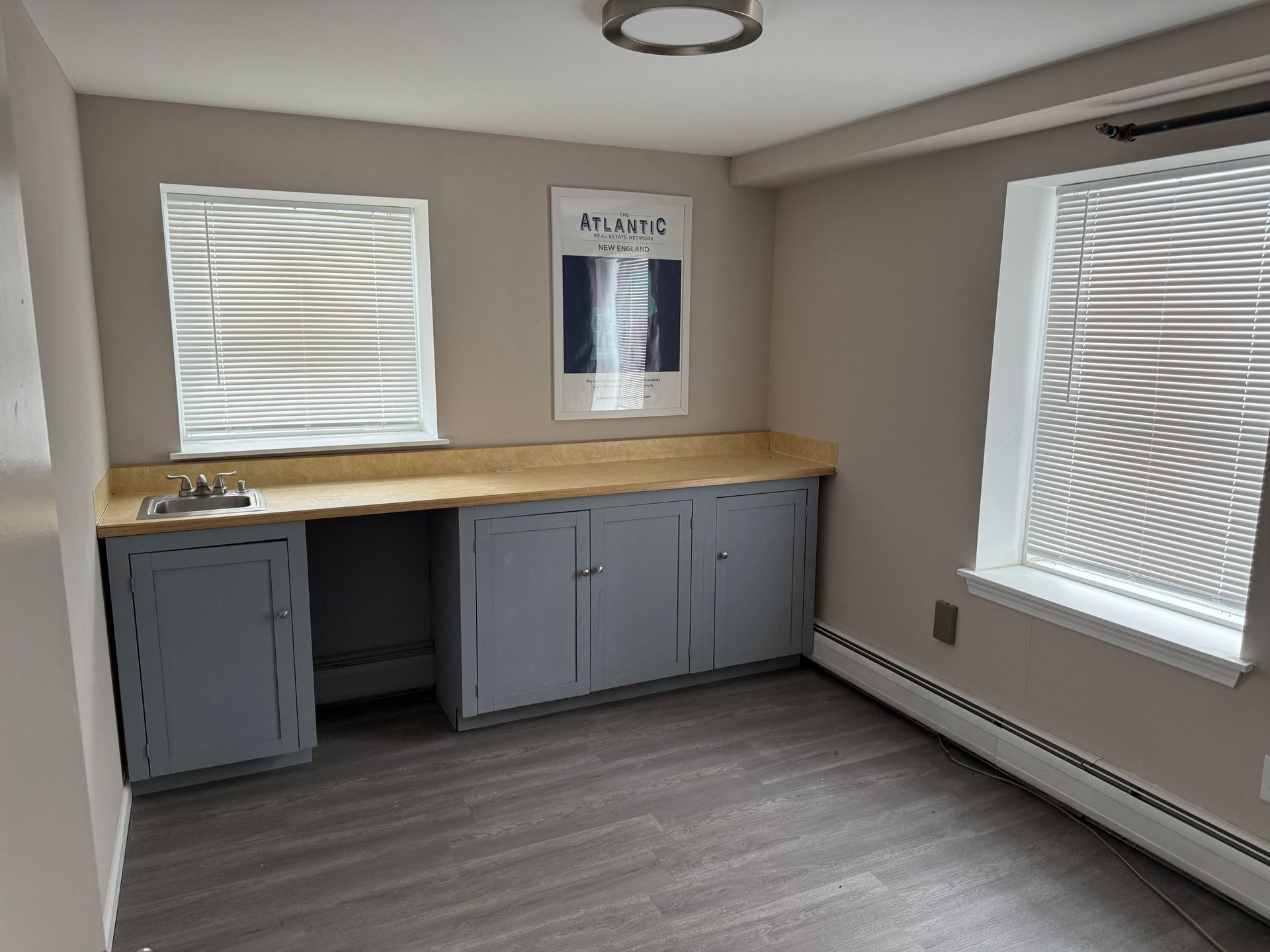Room with a built-in sink and cabinets. A window is on either side. Gray and beige tones.