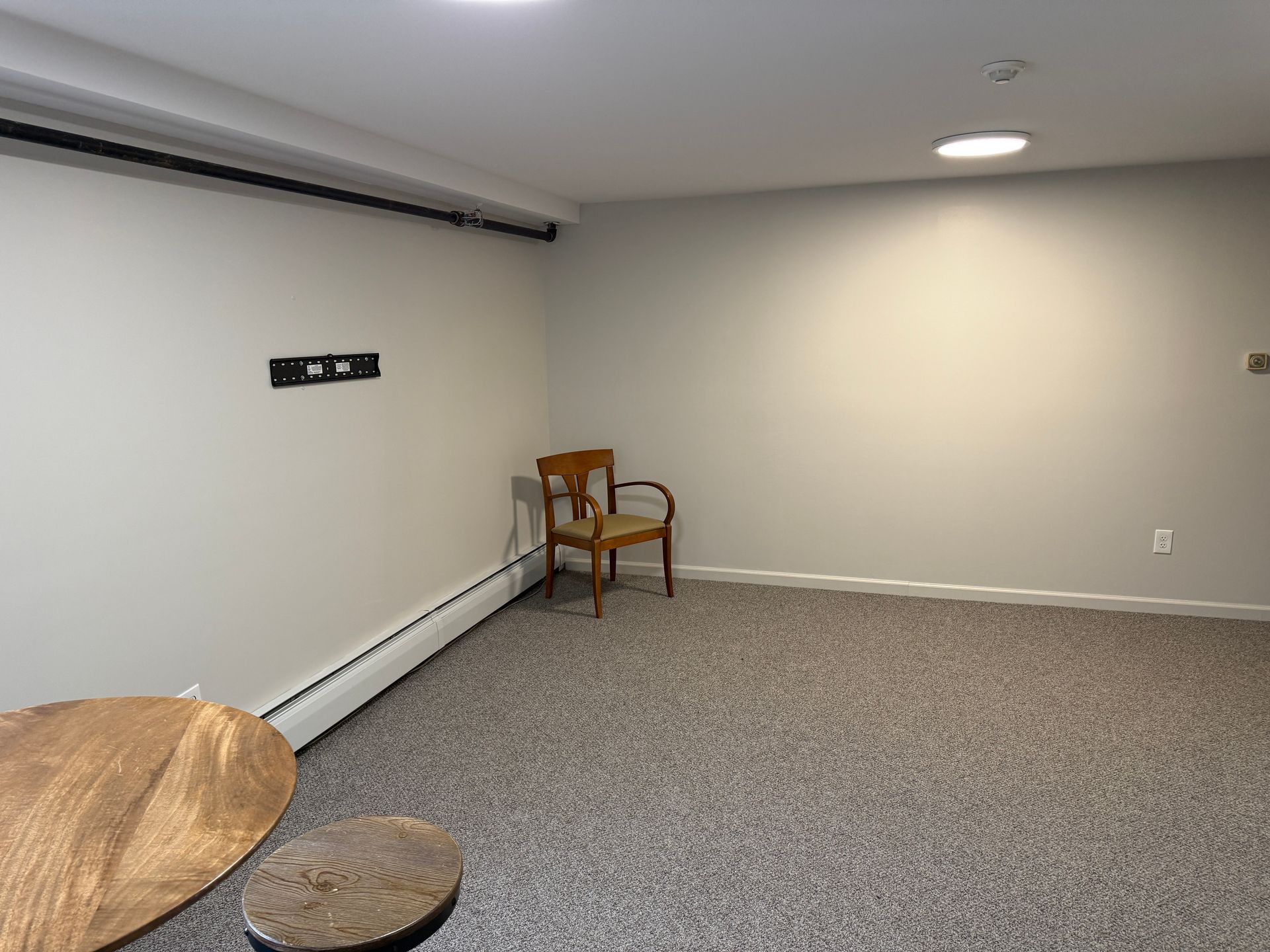 Empty room with gray walls, carpet, a chair, and two round wooden tables.
