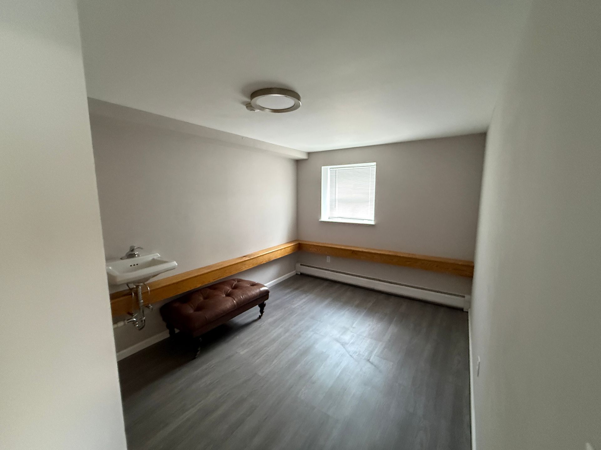 Empty room with gray walls, wood trim, window, and a small bench.