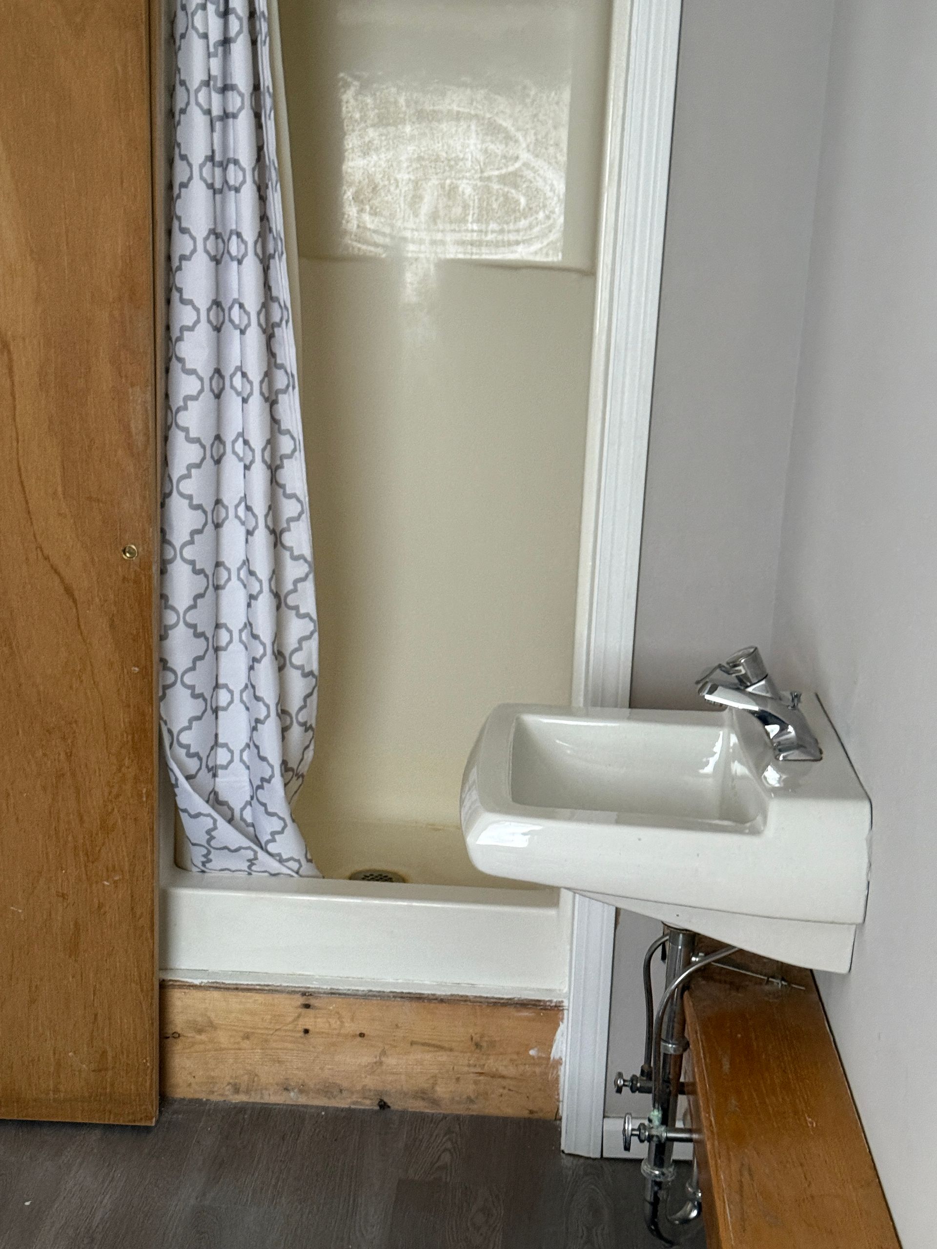 Small bathroom with shower/tub combo, wall-mounted sink, and wooden trim.