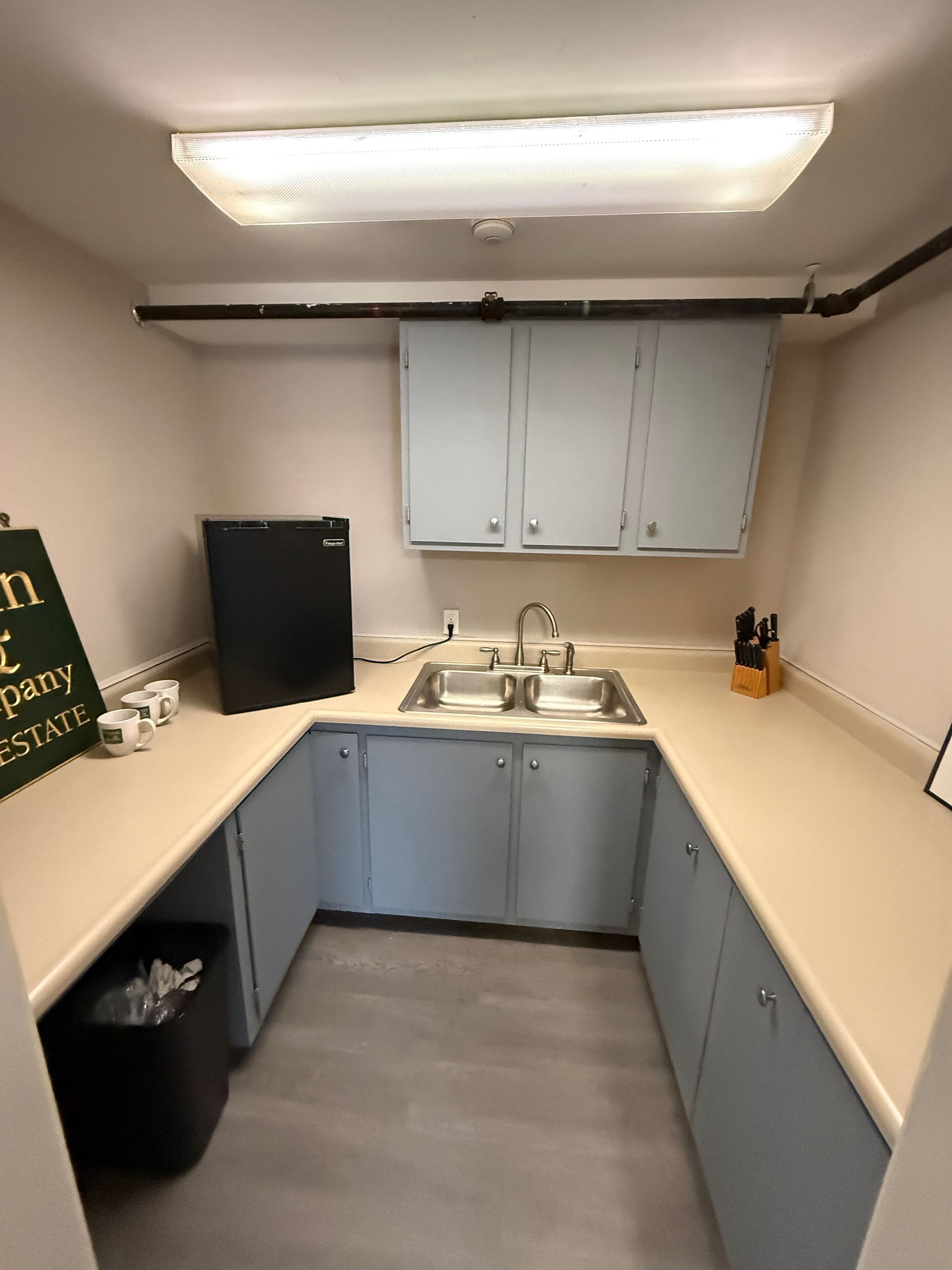 Small kitchenette with light blue cabinets, stainless steel sink, and a black mini-fridge.