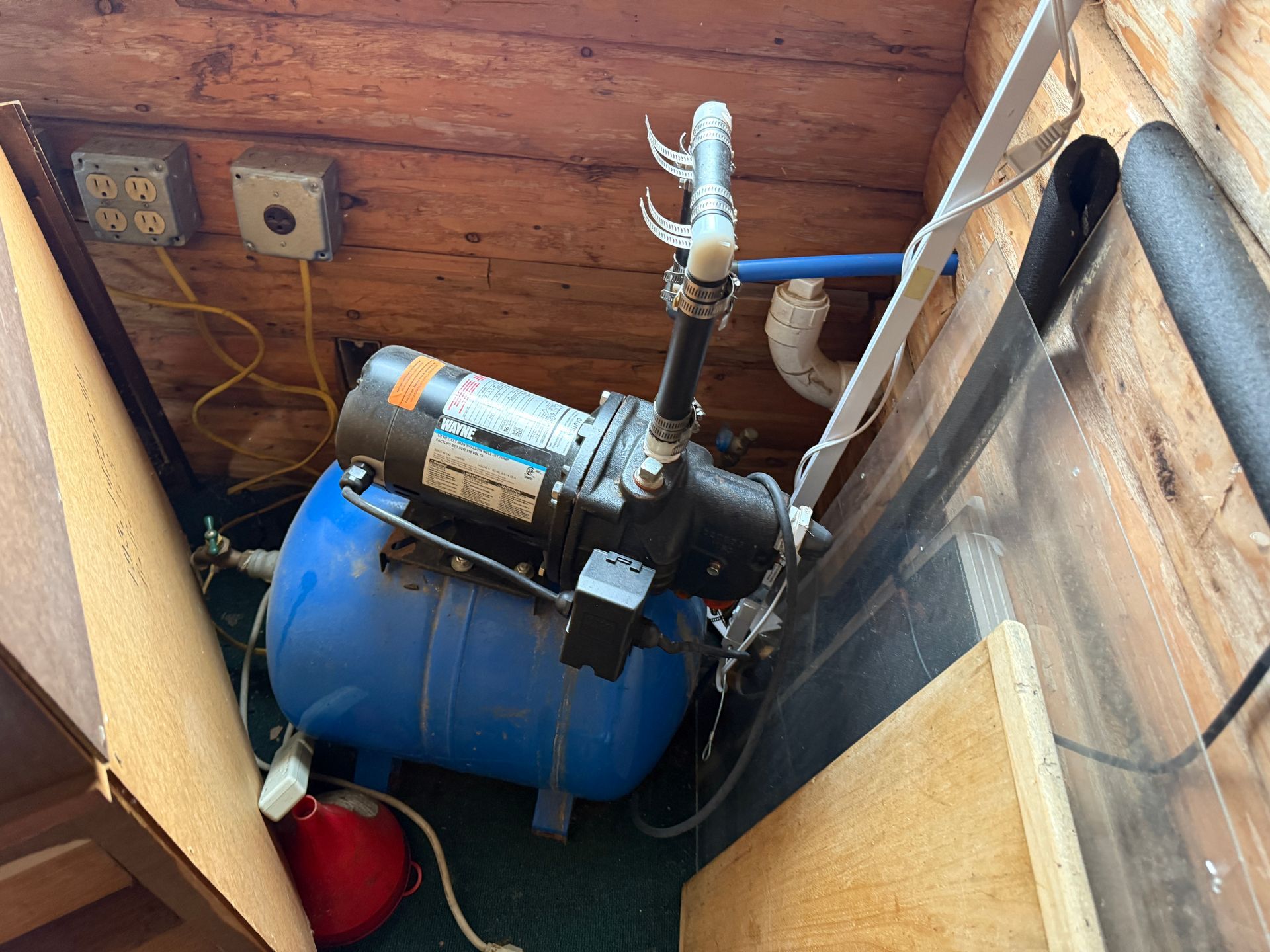 A water pump system with a blue tank, black pump, and electrical outlets installed in a wooden enclosure.