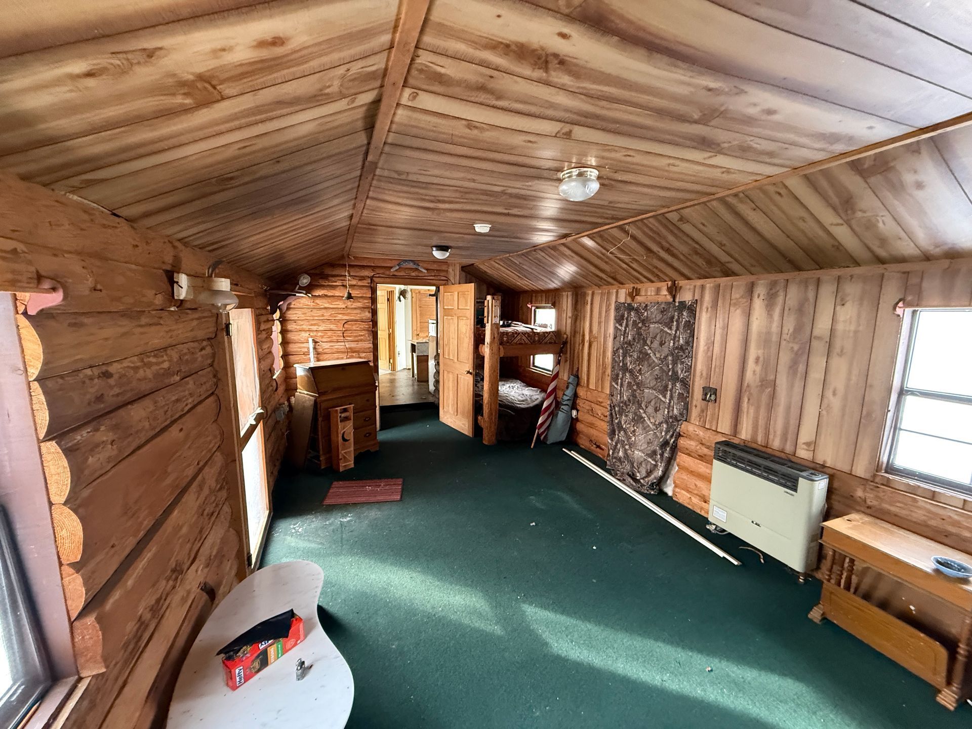 Interior of a wood-paneled cabin. Features a green carpet, bunk beds, and a white table.