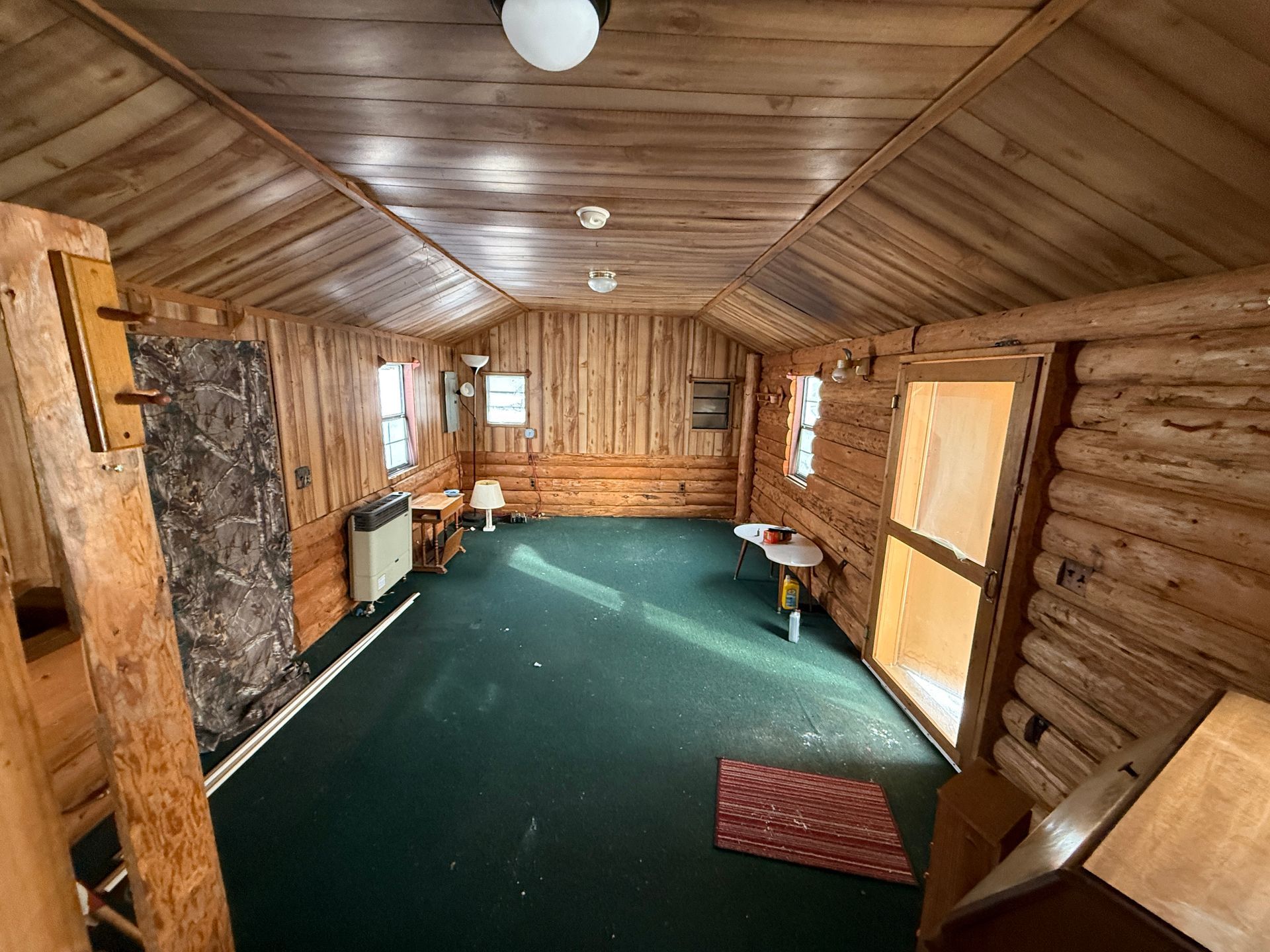 Interior of a wooden cabin with a green carpet, windows, and a partially open door.