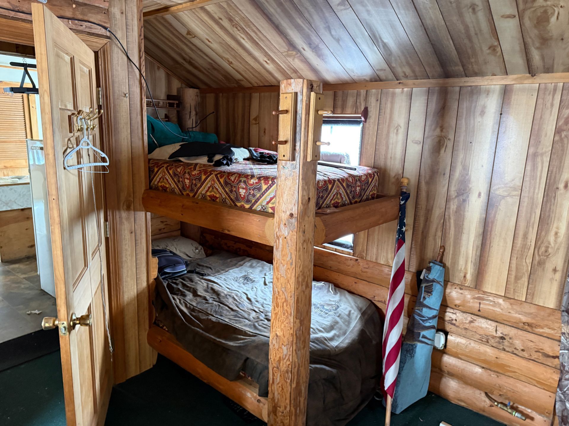 Bunk beds in a small cabin. Wooden frame, two beds stacked, American flag on the right.