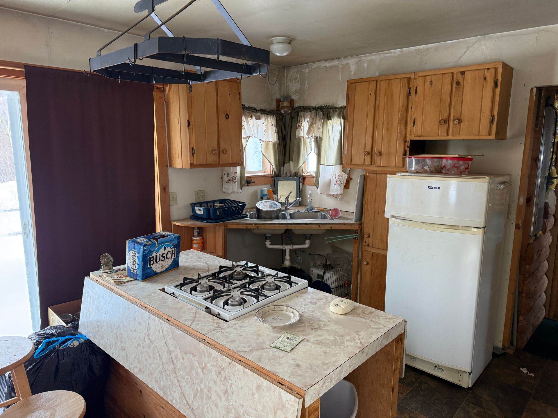 Kitchen with wood cabinets, island with stovetop, old refrigerator, and a dark purple wall.
