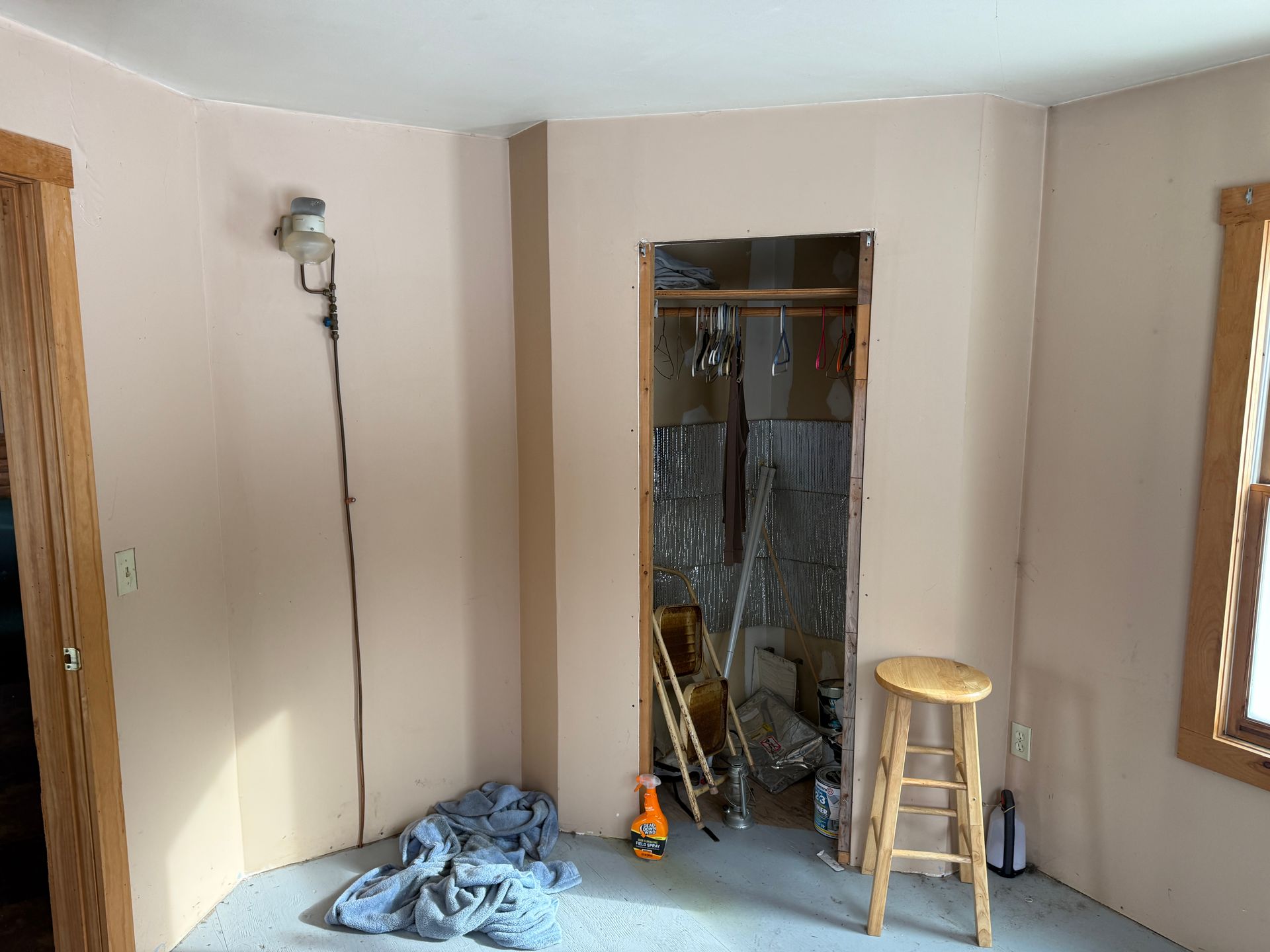 Room with closet, walls are tan and bare. A stool and tools sit inside.